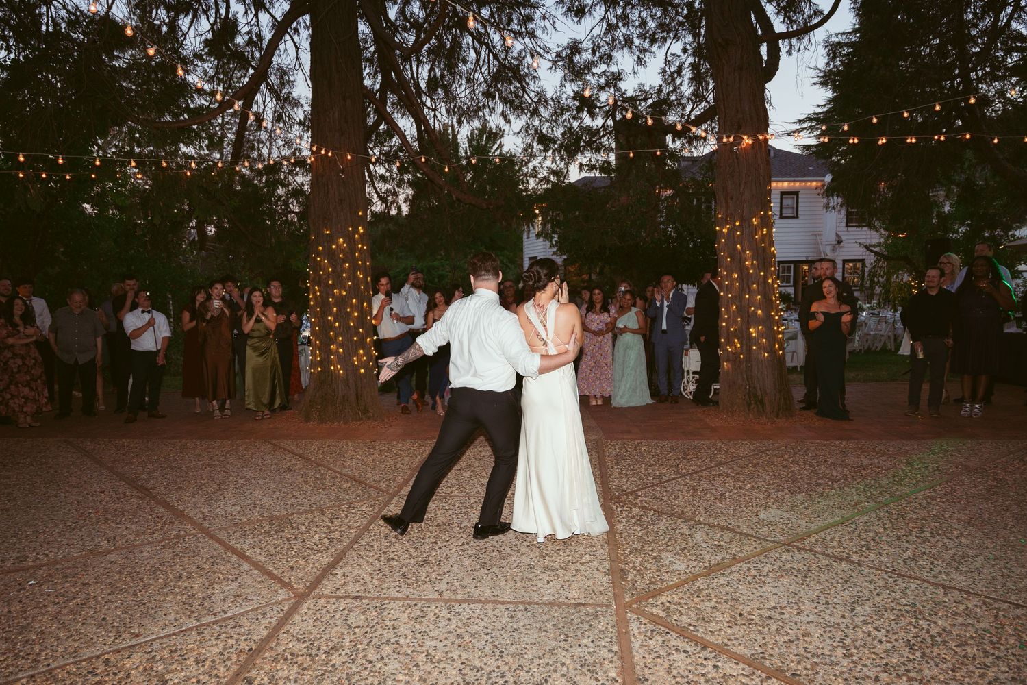 Couple shares their first dance under twinkling lights at outdoor evening reception.