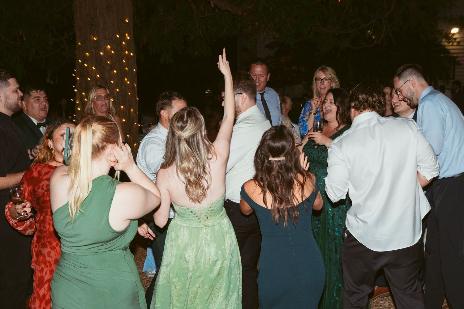 Wedding guests dancing and celebrating under string lights at outdoor reception.