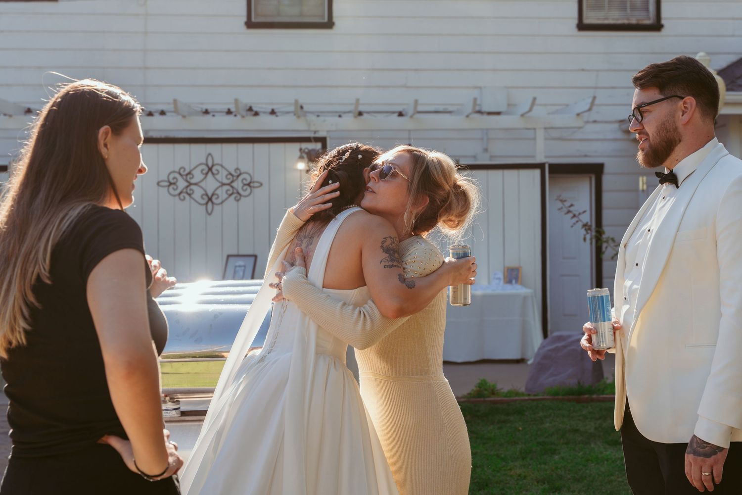 Wedding party members pose together outside a white building in formal attire.