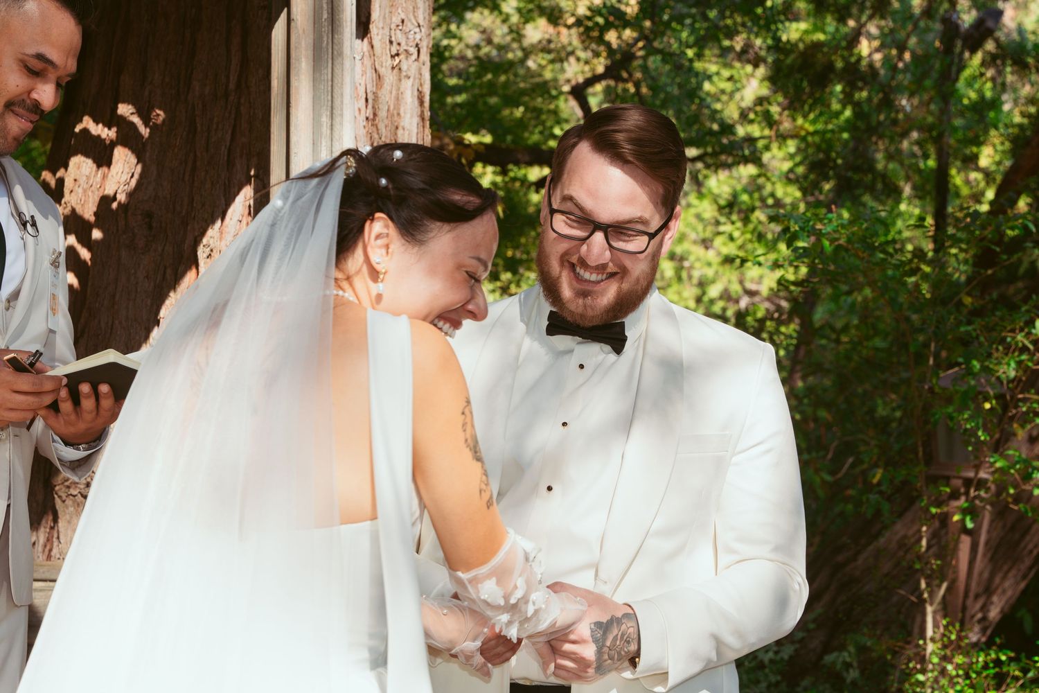 A couple shares an emotional moment during their wedding ceremony under a wooden pergola surrounded by greenery.