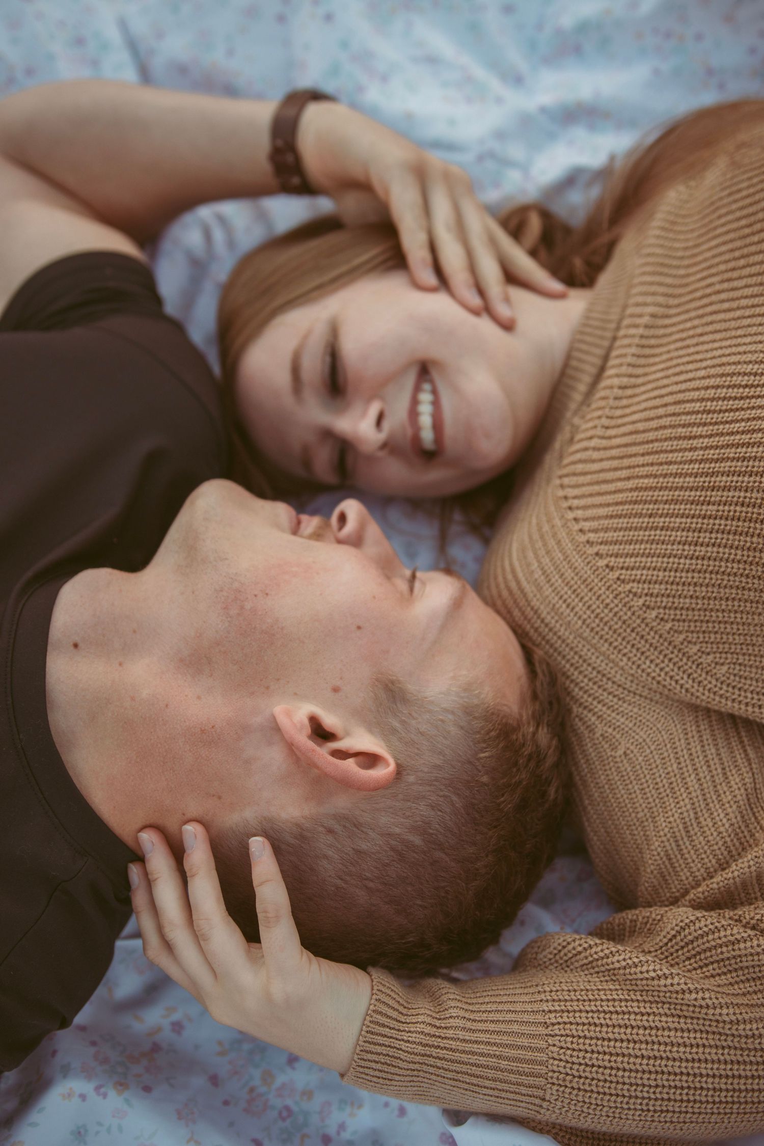 Close up of couple sharing intimate laughter while laying on blanket outdoors.