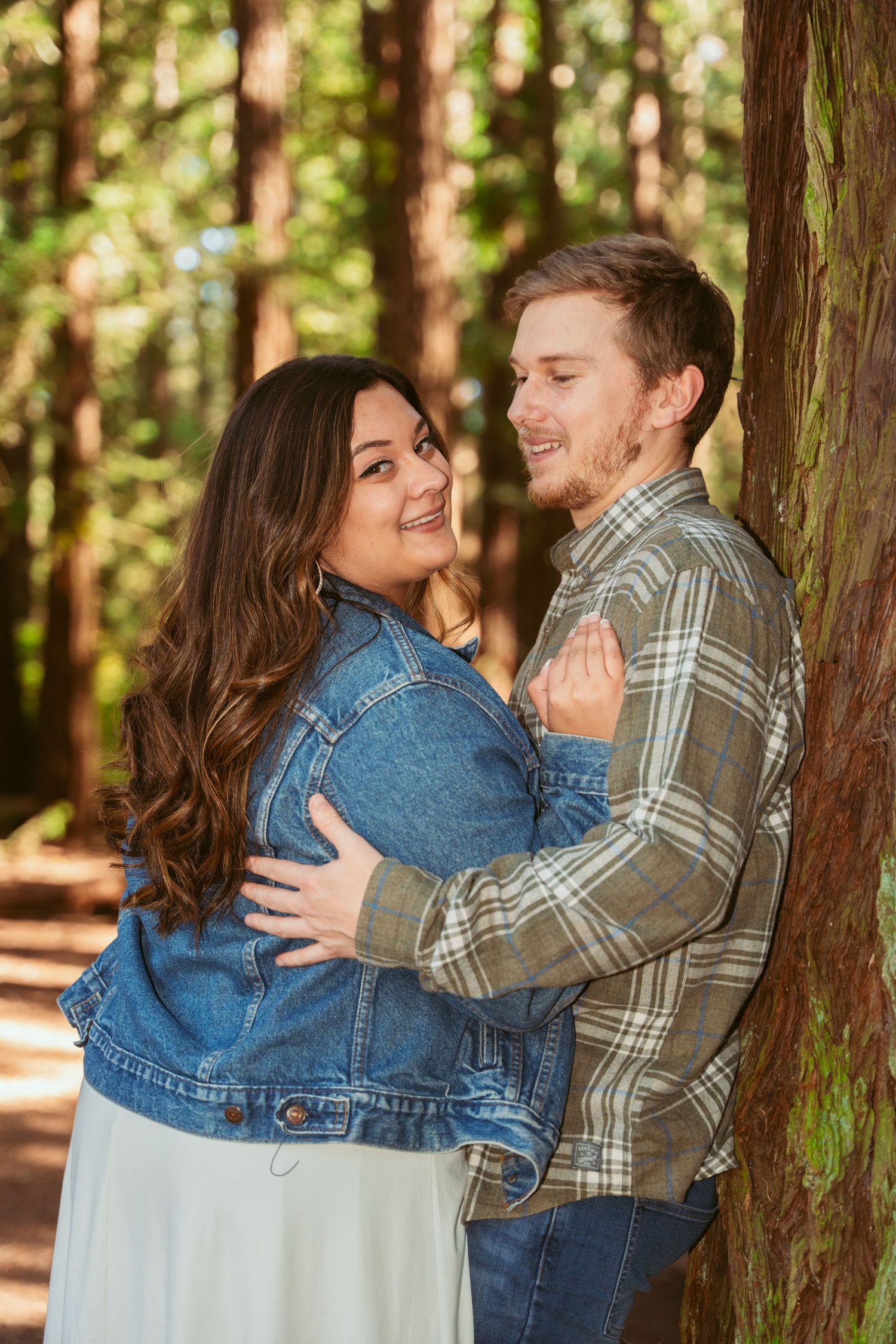 Romantic embrace among tall trees in sunlit forest setting.
