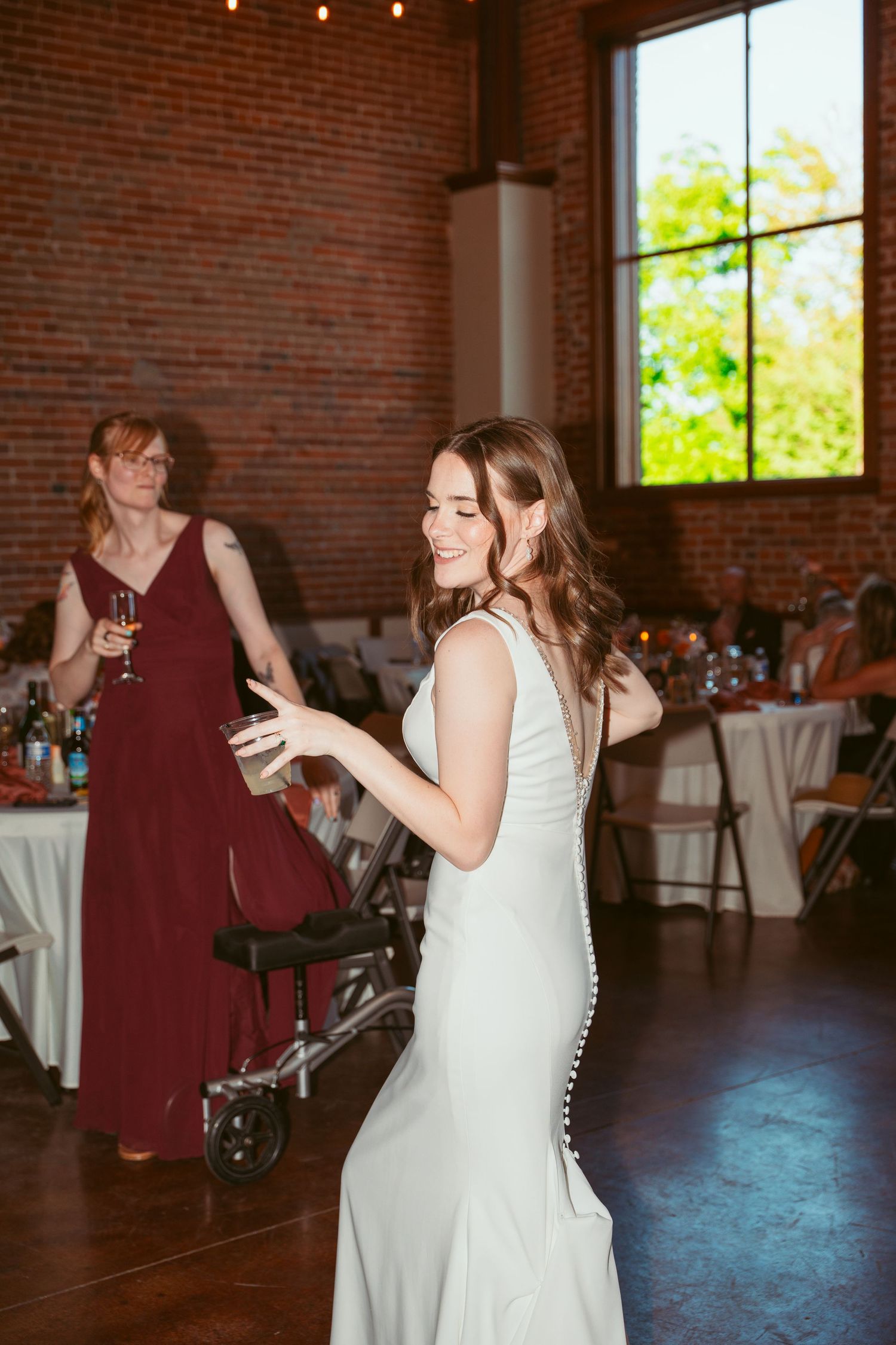 Dancers enjoying themselves at a wedding reception in a bright brick-walled venue with tall windows.