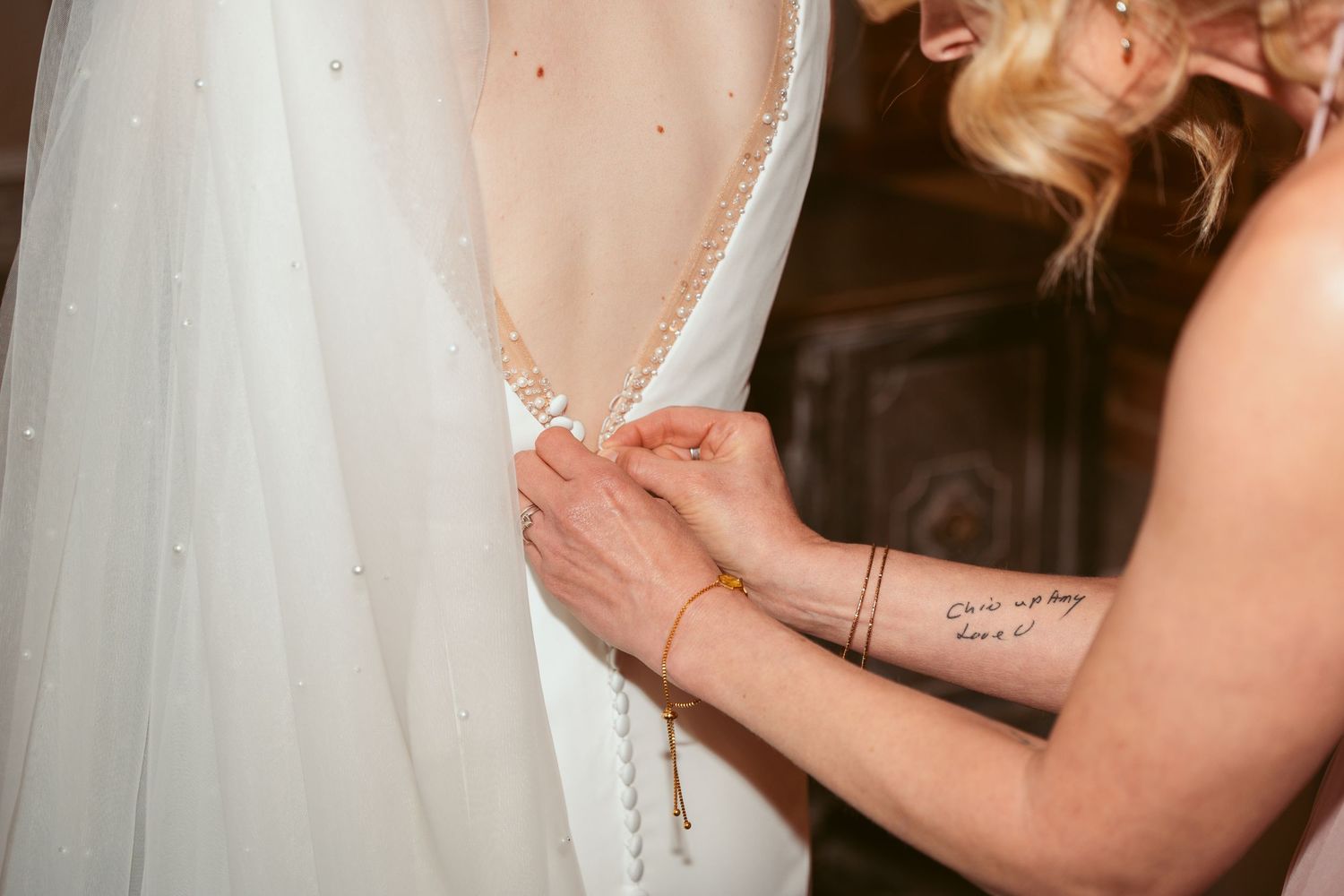 Detail shot of white wedding dress being secured in vintage brick venue.