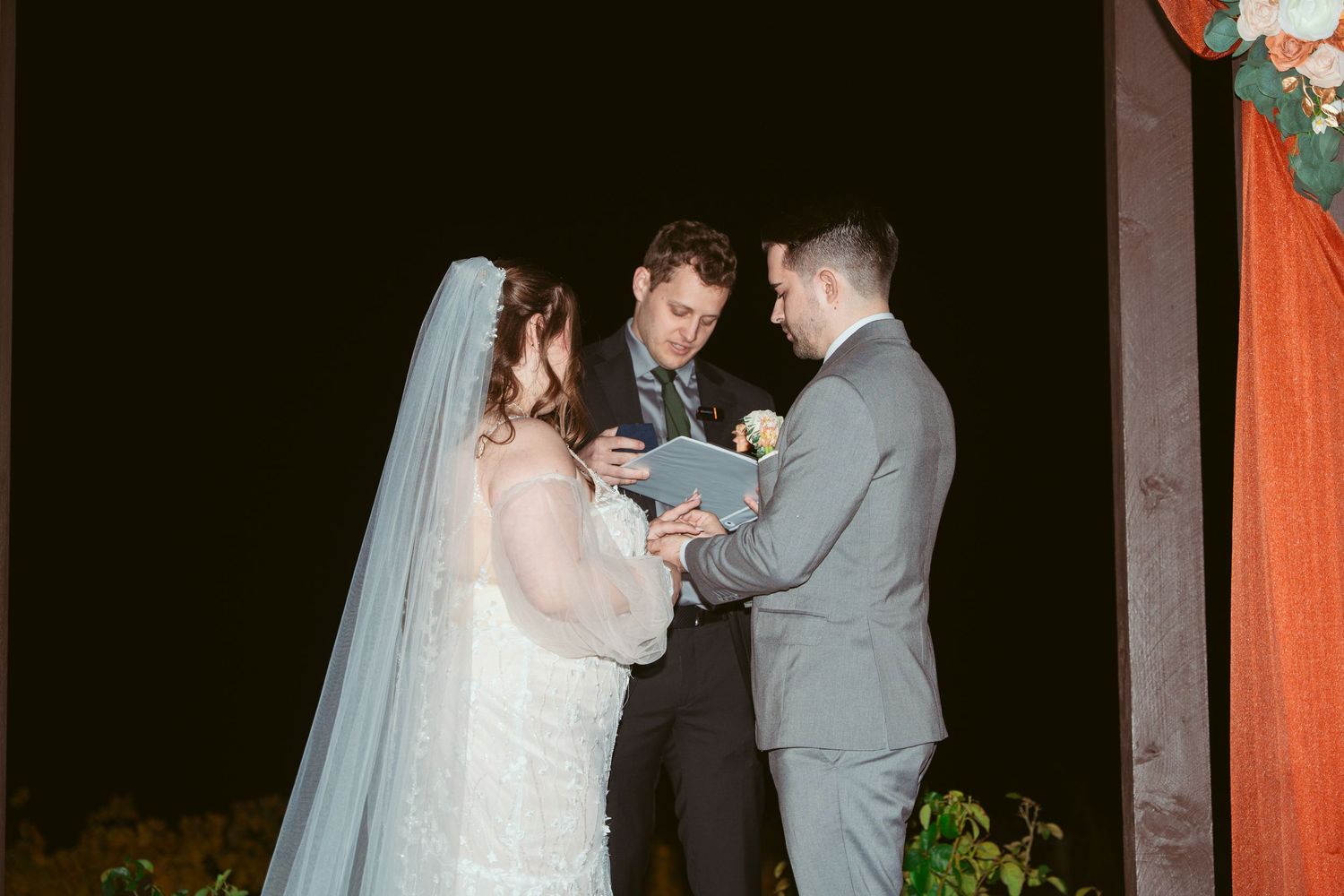 Couple sharing intimate moment during nighttime wedding ceremony under decorated arch.