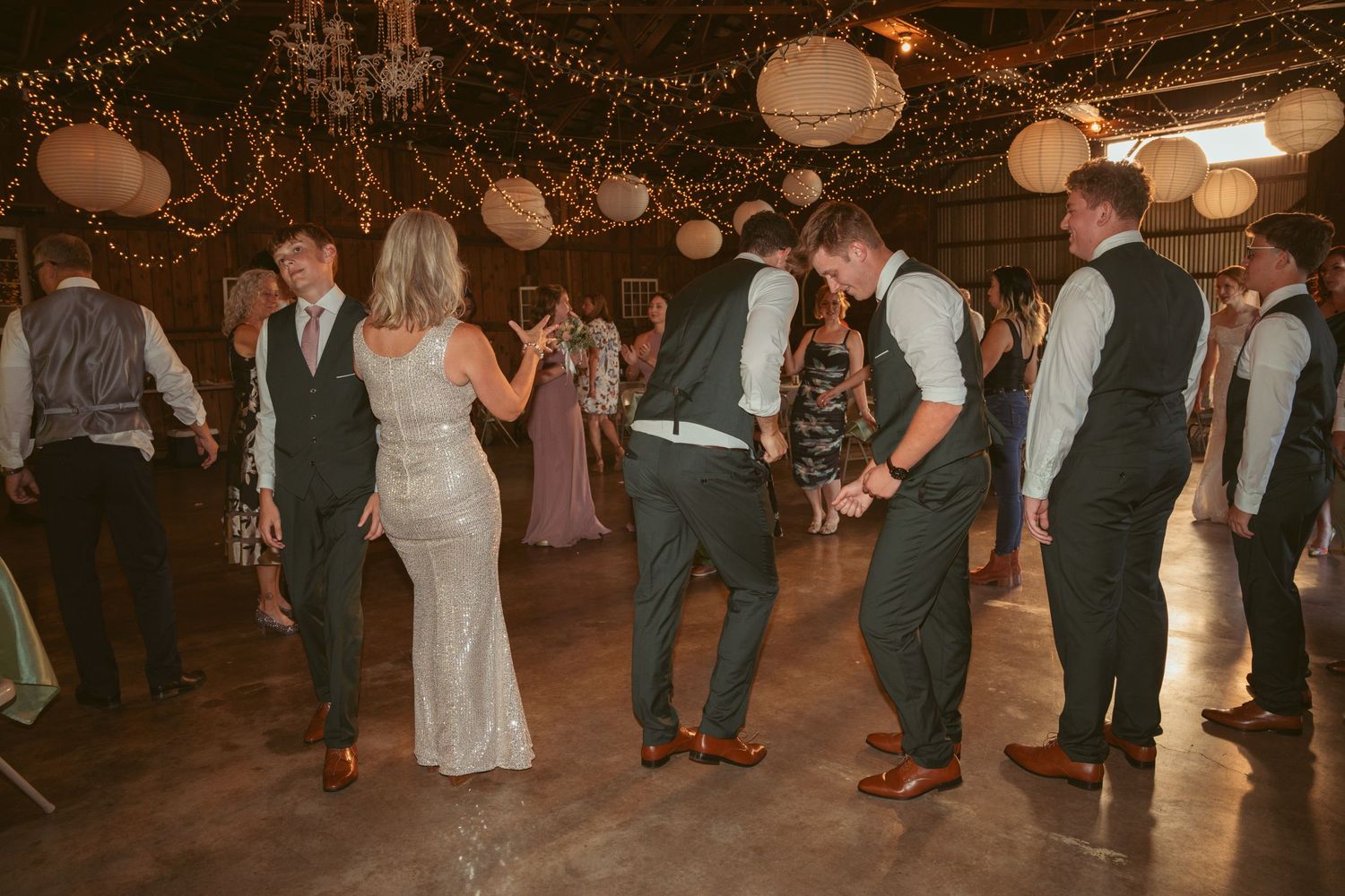 Guests dancing and celebrating at a rustic barn wedding reception with string light decor.