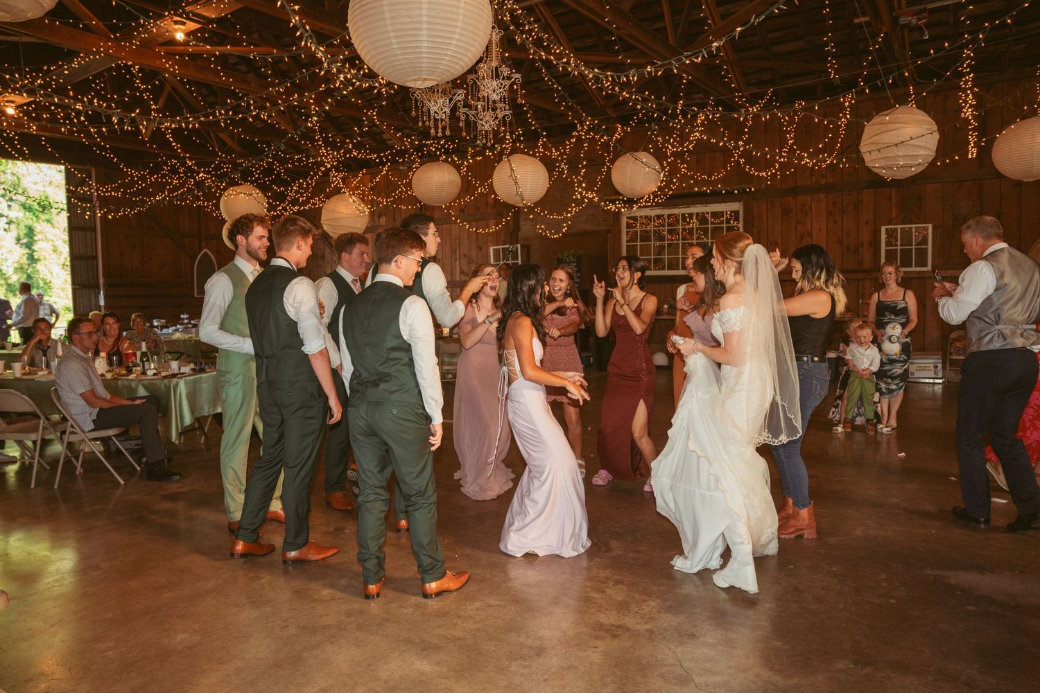 Wedding party dances and celebrates on a wooden dance floor under glowing lanterns and twinkle lights.