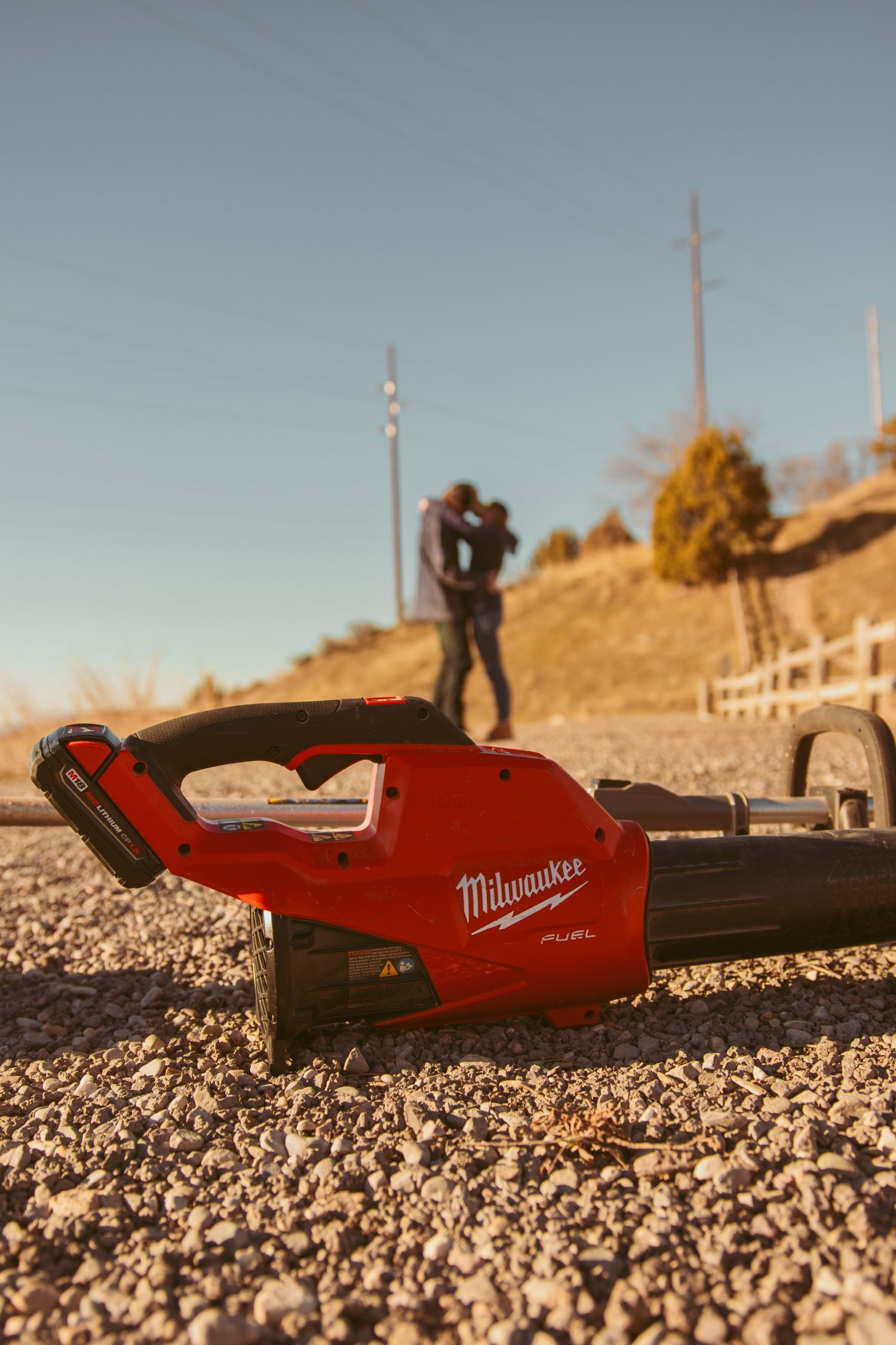 A red Milwaukee power tool lies on rocky ground with mountains in the background.