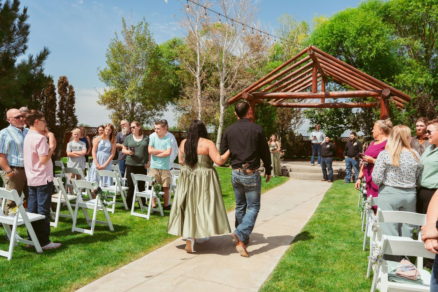Outdoor wedding venue with wooden pergola and white chairs arranged on grassy lawn.