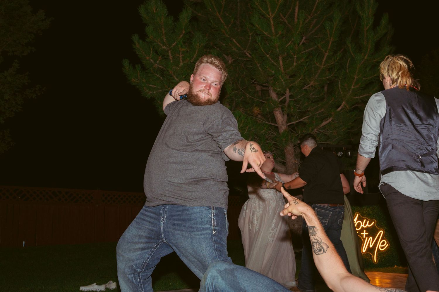 Wedding party dancing under string lights at an outdoor nighttime reception.