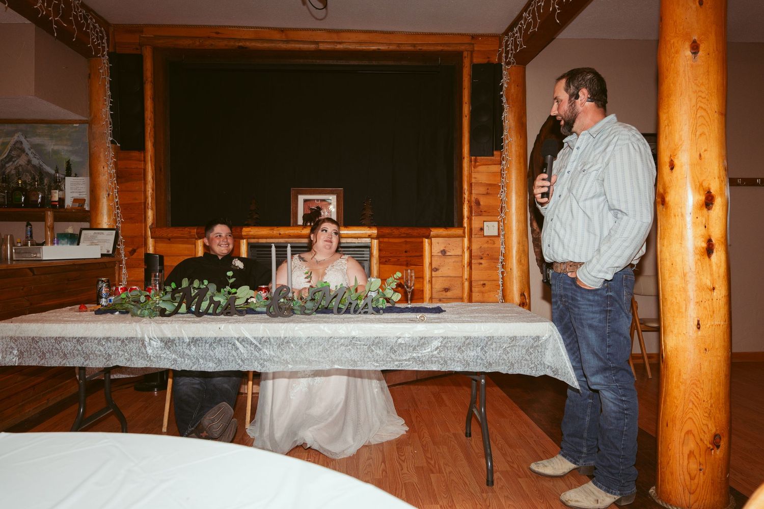 Wedding reception setup in a rustic lodge with wooden beams and decorative greenery.