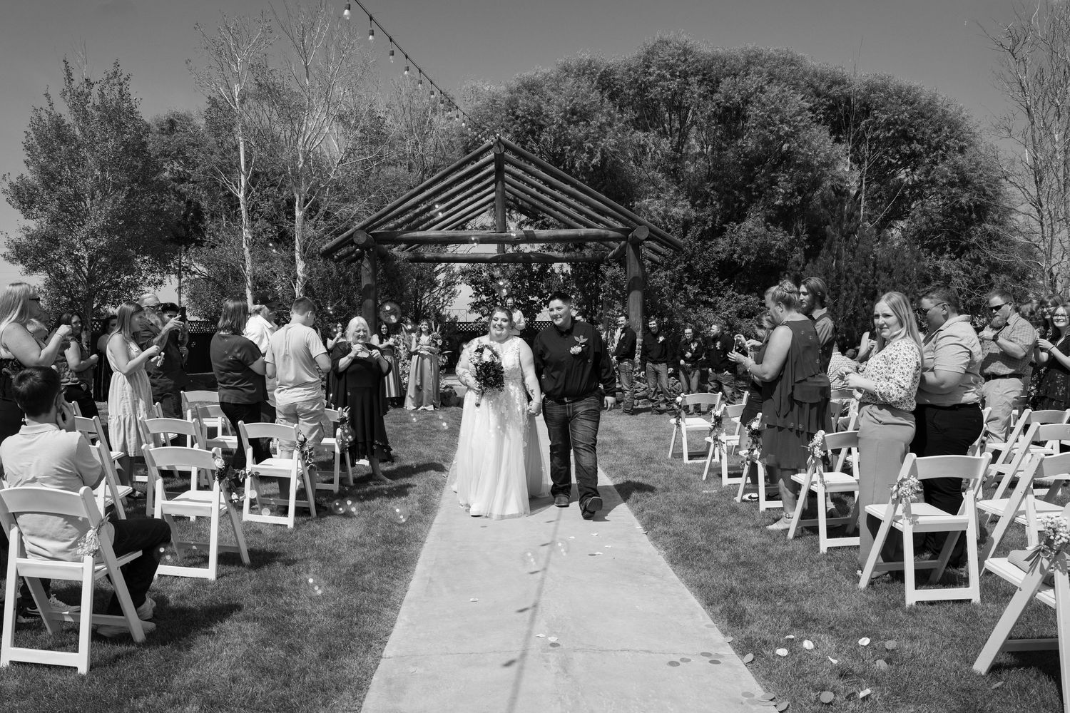 Black and white photo showing outdoor wedding ceremony seating with white chairs arranged in rows.