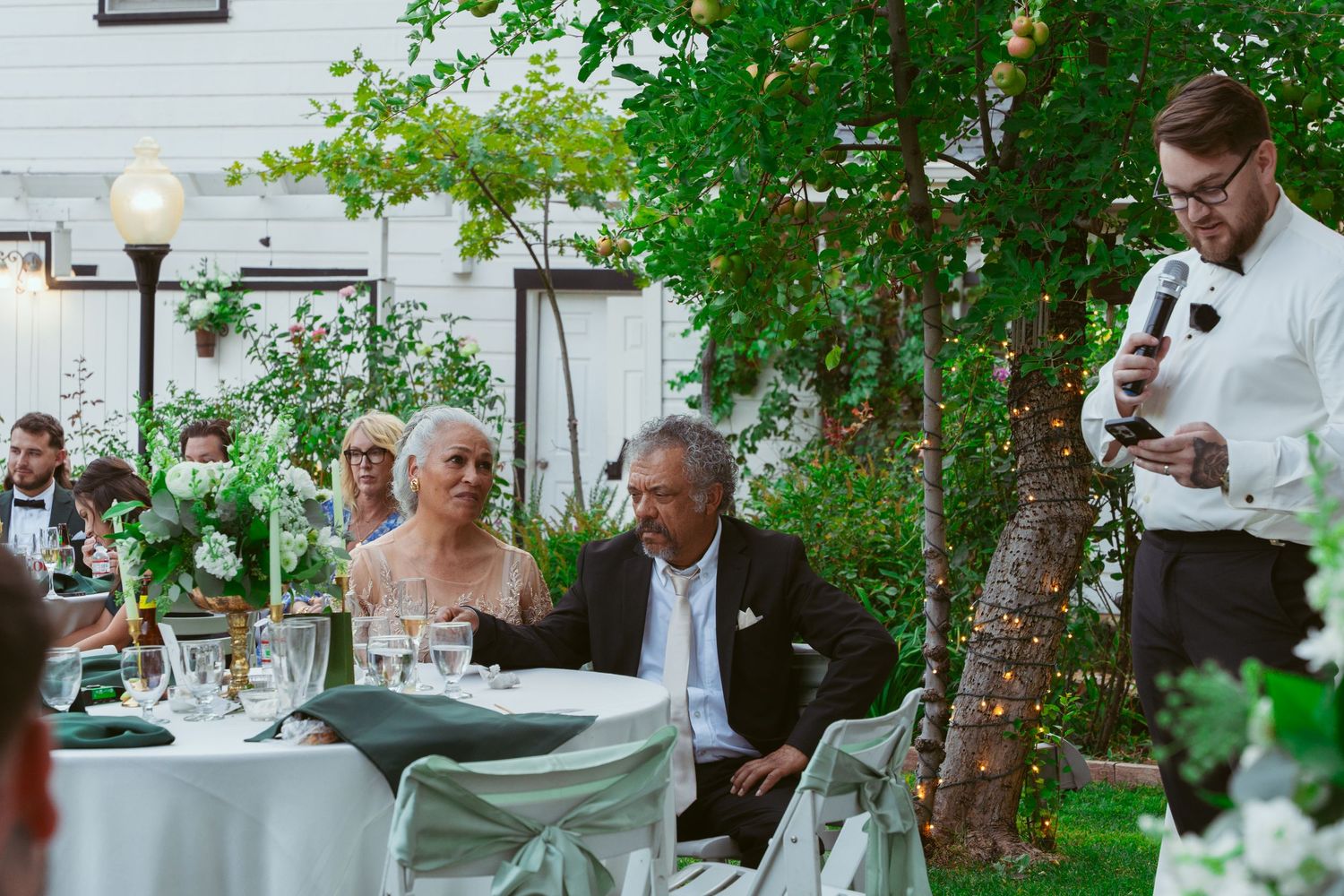 Guests mingling at an outdoor garden wedding reception with white tables and greenery.