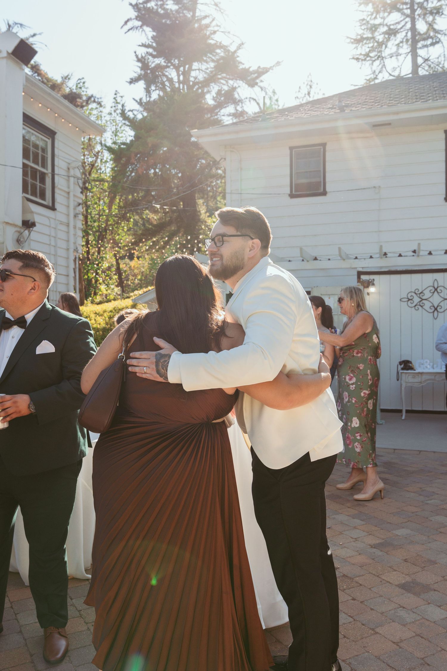 Wedding guests dancing in pairs on a brick patio outside a white building.