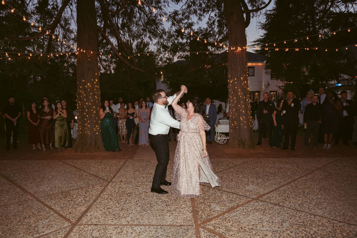 Wedding guests dance beneath glowing string lights at a romantic outdoor reception.