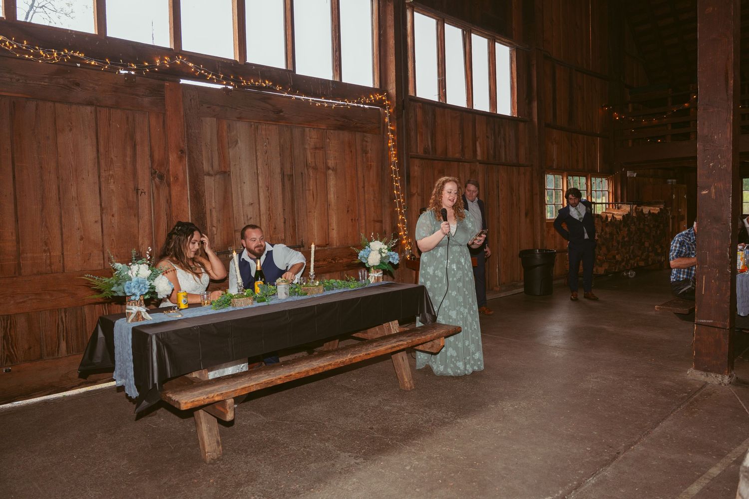 Wide angle view of a rustic barn wedding reception space with wooden benches and tables.