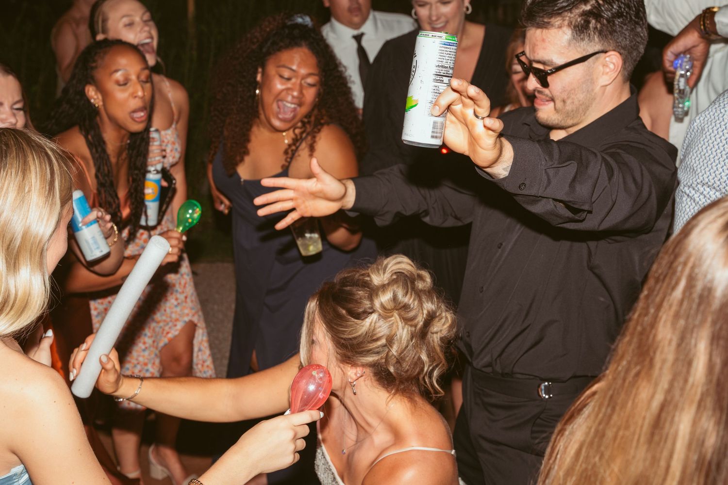 Energetic party guests dance and celebrate with drinks at a nighttime wedding reception.
