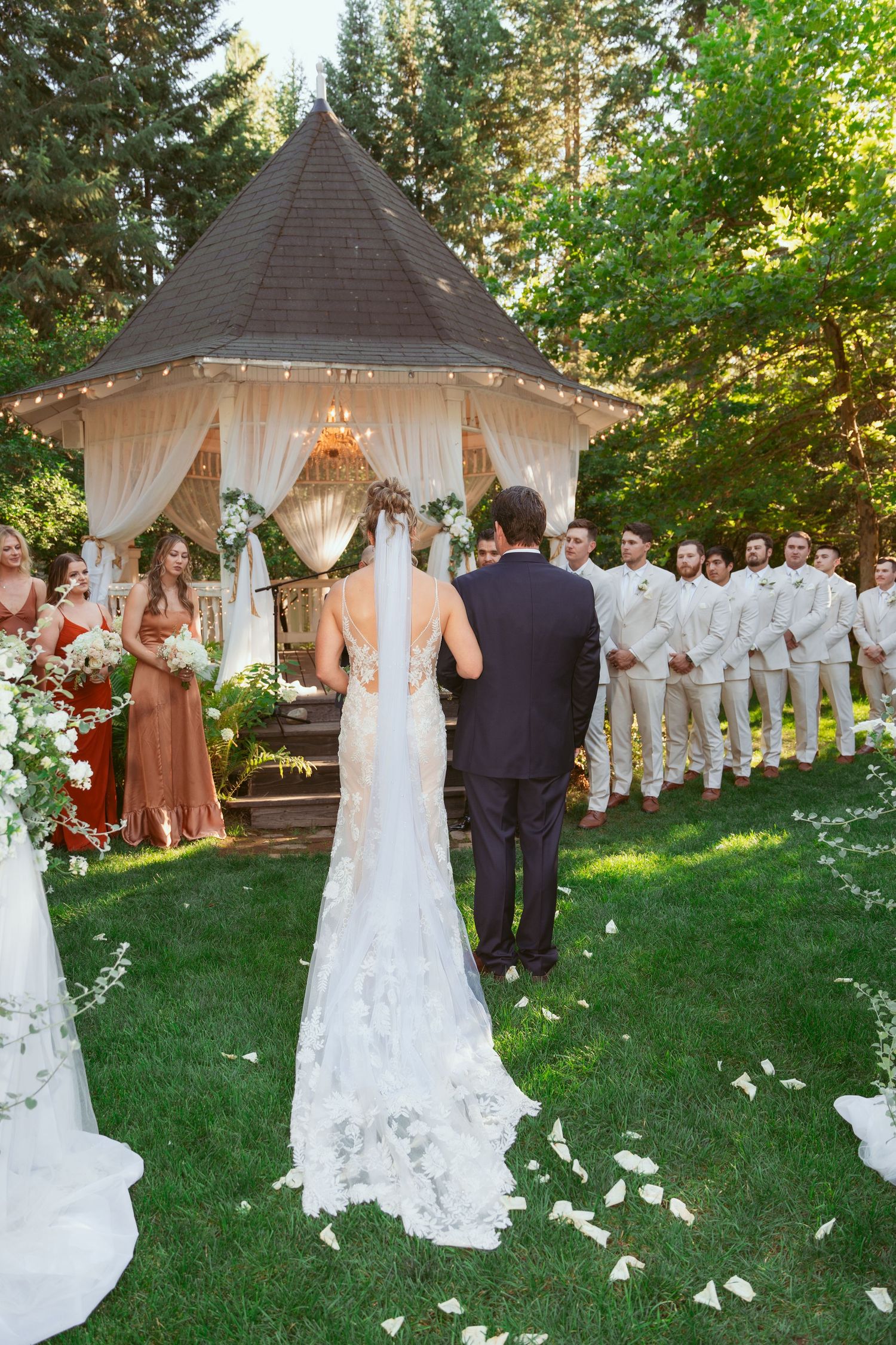 Outdoor wedding ceremony under a gazebo decorated with flowing white fabric and floral arrangements.