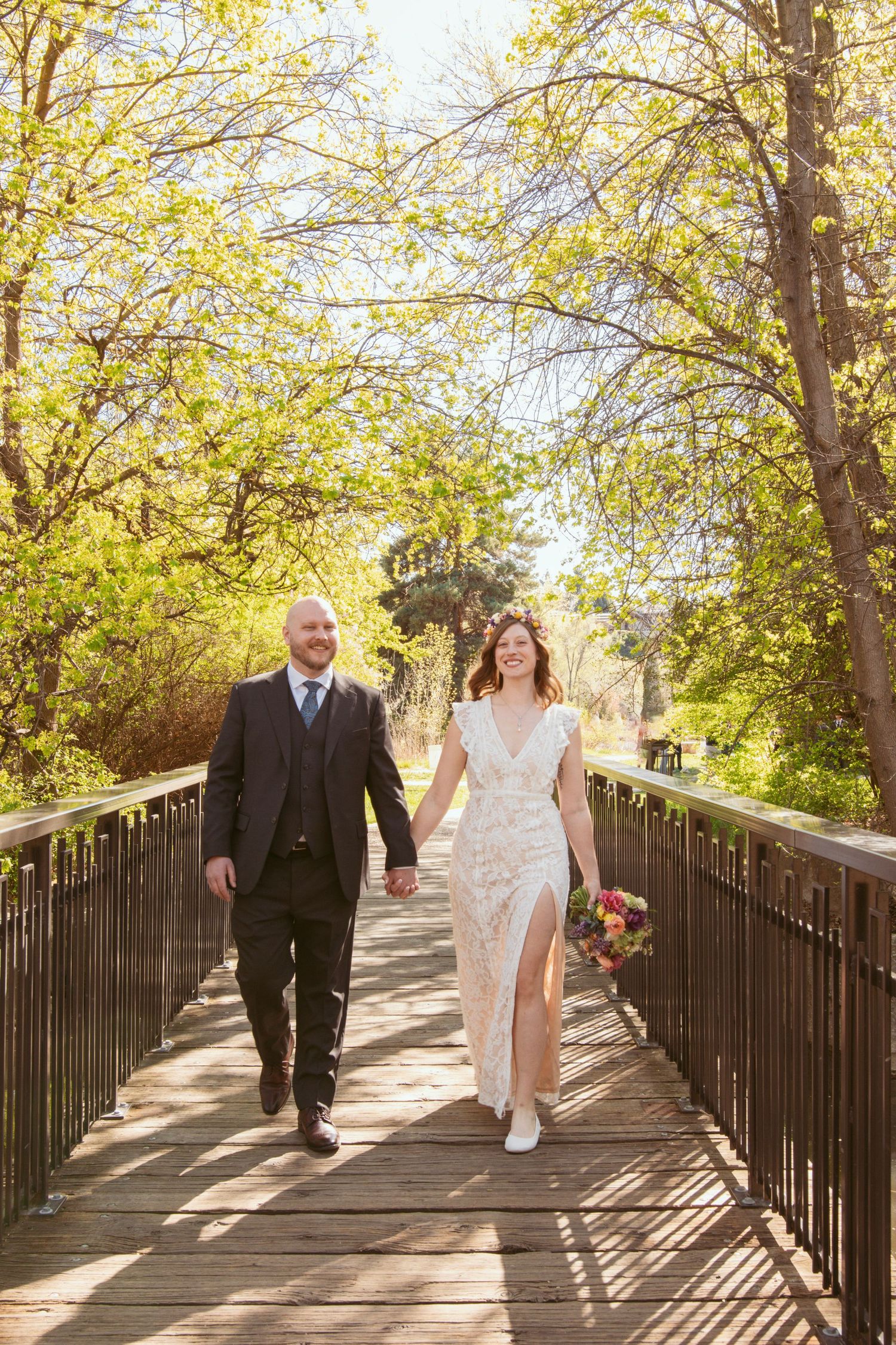 Wedding party walking along sunny wooden boardwalk surrounded by spring foliage.