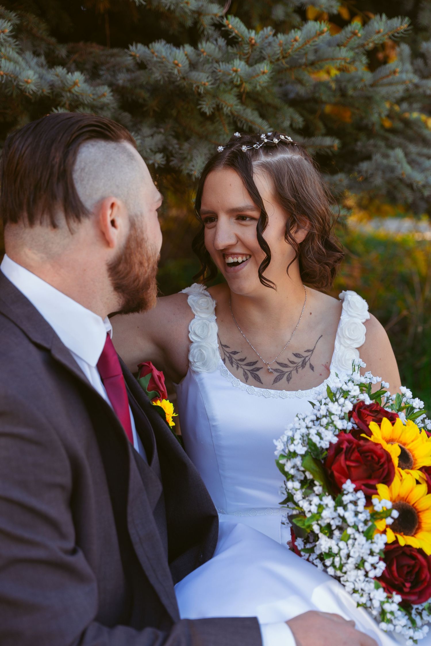 Romantic wedding portrait with sunflower bouquet and red roses against blue spruce trees.