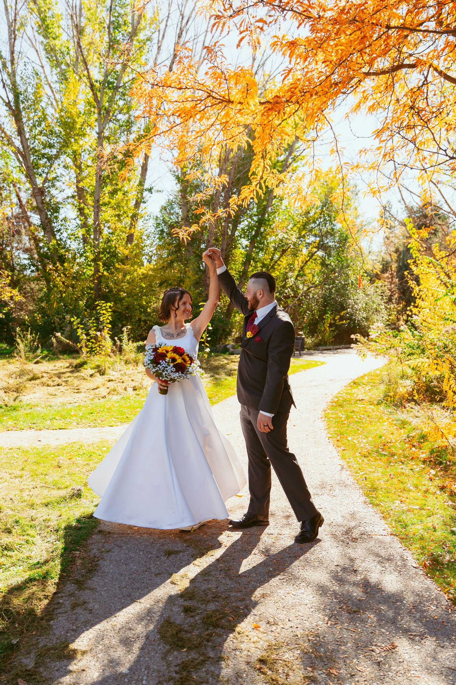 A couple performs a romantic dance move on a path lined with autumn trees.