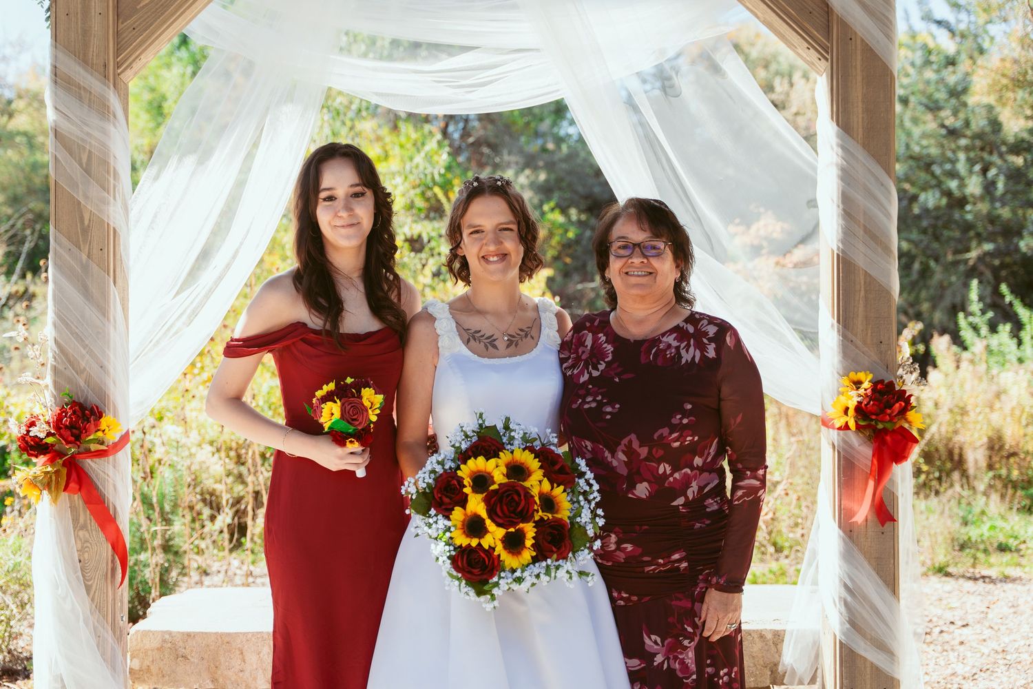 Outdoor wedding ceremony setup with white draping and burgundy floral decorations.