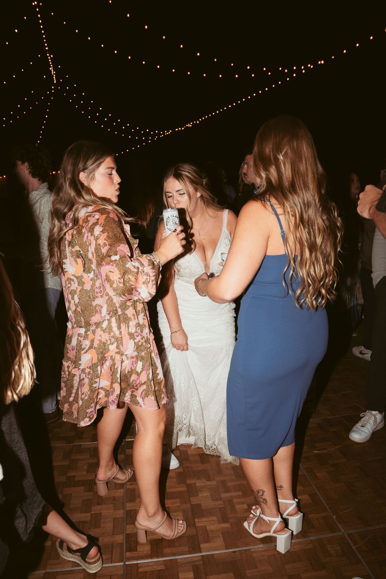 Wedding guests dancing together on a wooden dance floor during an evening celebration.