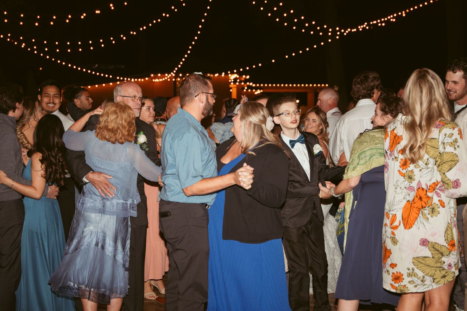 Couples dancing beneath glowing string lights at a festive outdoor wedding reception.