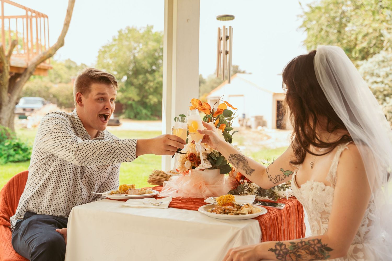 A romantic wedding scene with a couple embracing outdoors on a sunny autumn day with orange and white floral decorations.