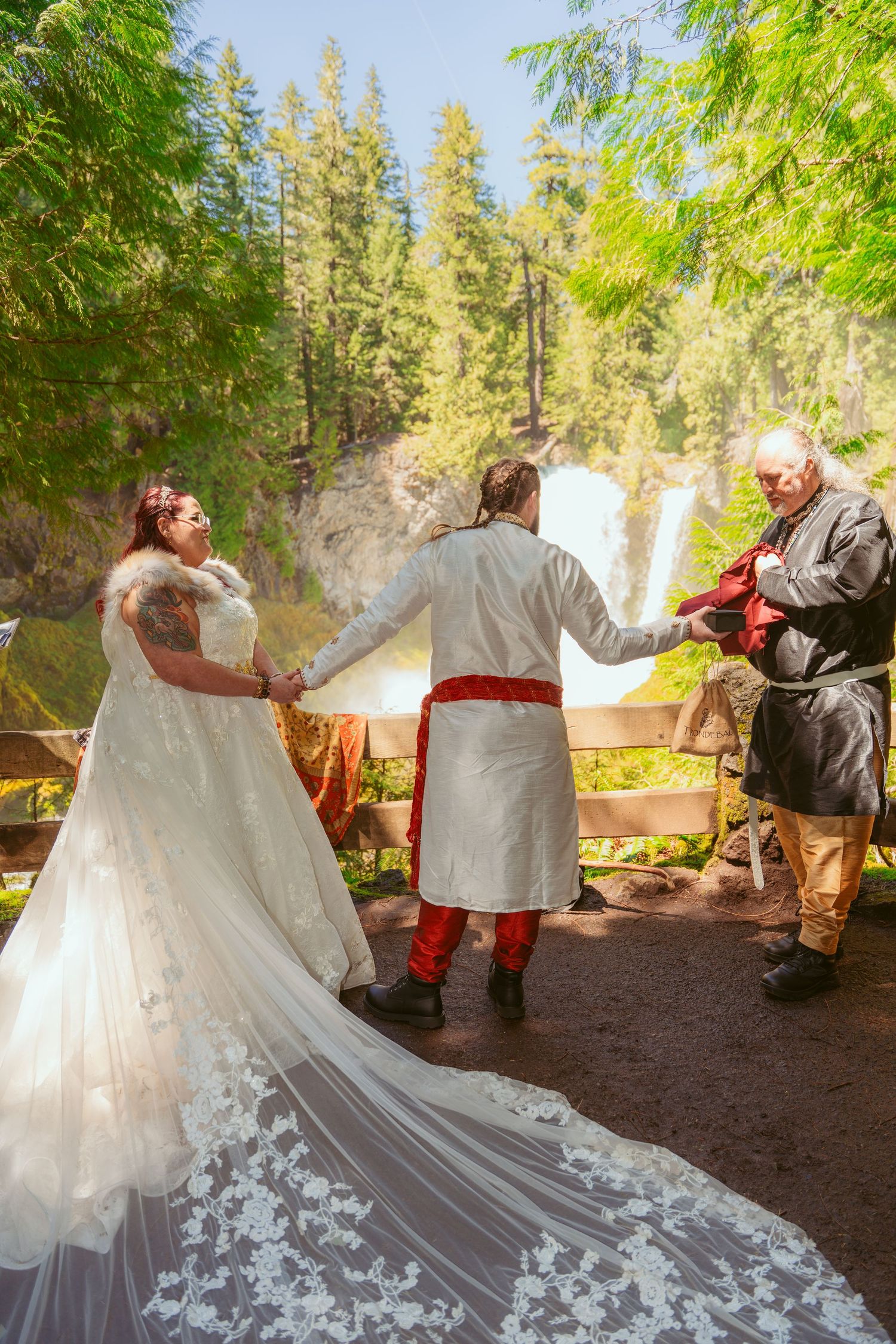 Wedding dress with intricate lace train against forest path backdrop.