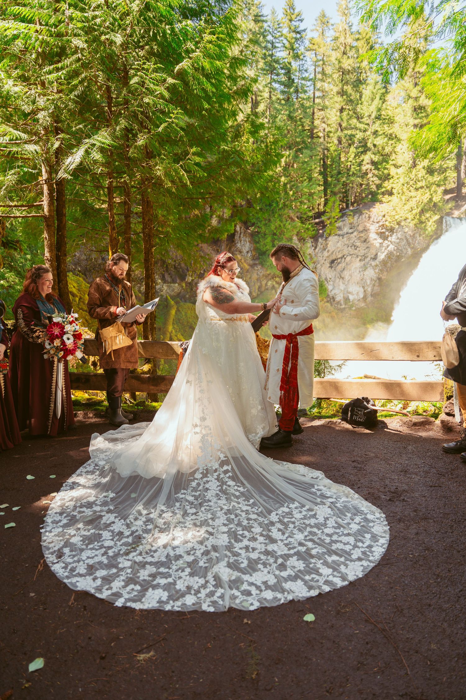 A wedding ceremony in a forest with a stunning lace train dress and waterfall backdrop.