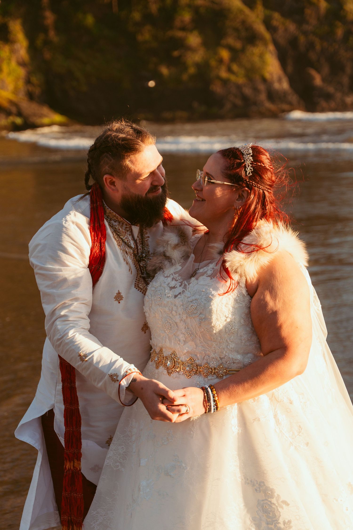 Wedding couple sharing intimate moment on beach with rocky coastline in background.