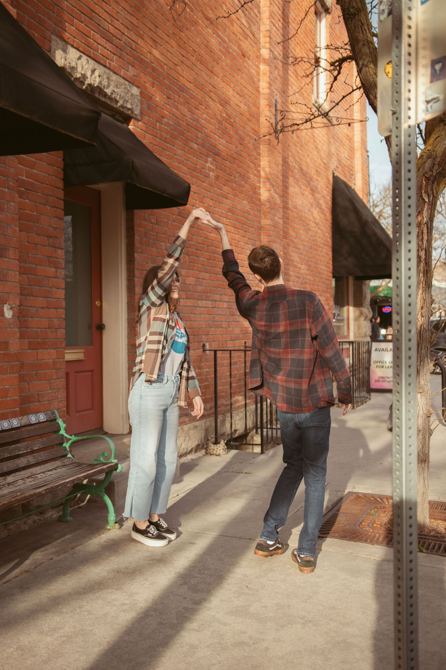 A couple dances together on a sunny sidewalk beside a brick building.