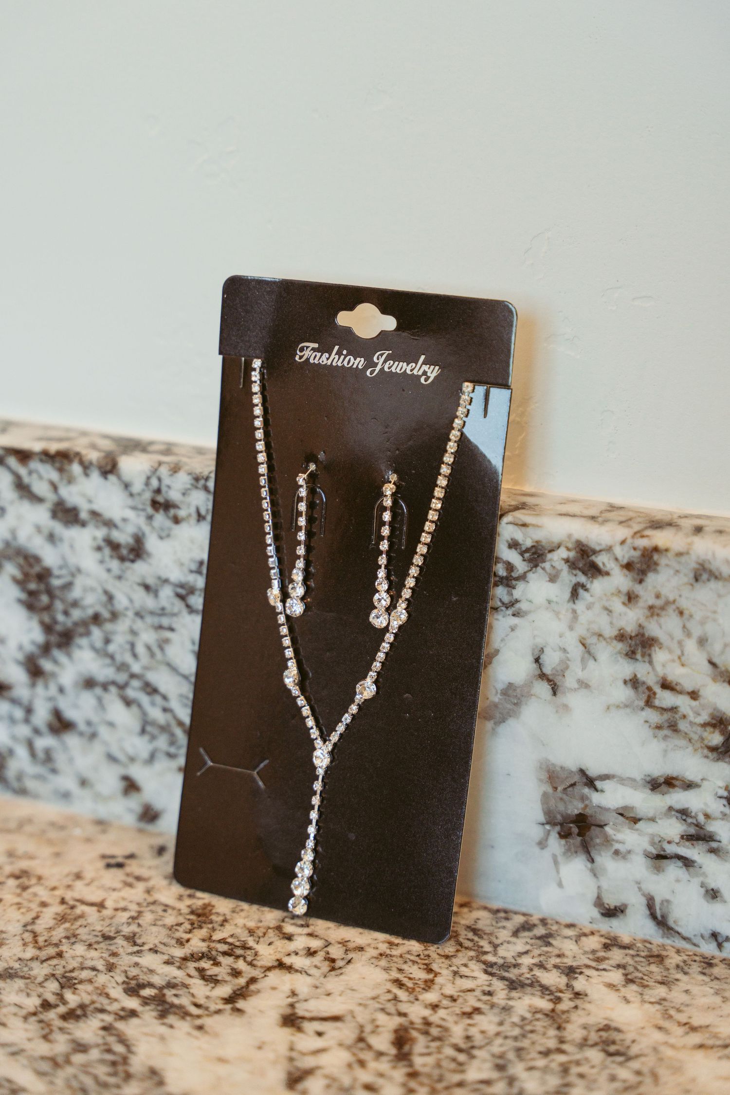 Sparkly rhinestone jewelry displayed on black display cards against marble countertop.