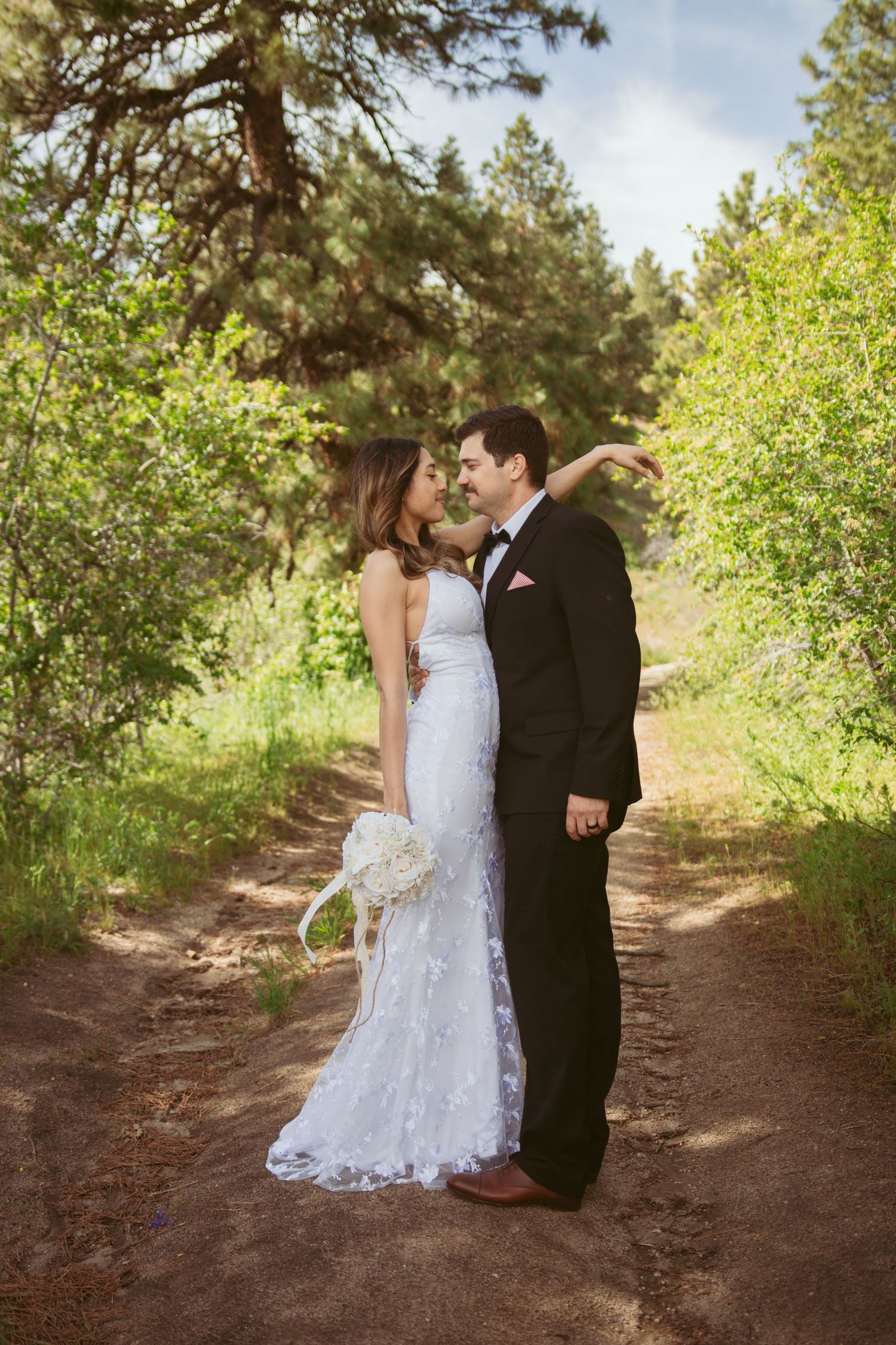 A romantic wedding moment captured on a forest trail with lush greenery.