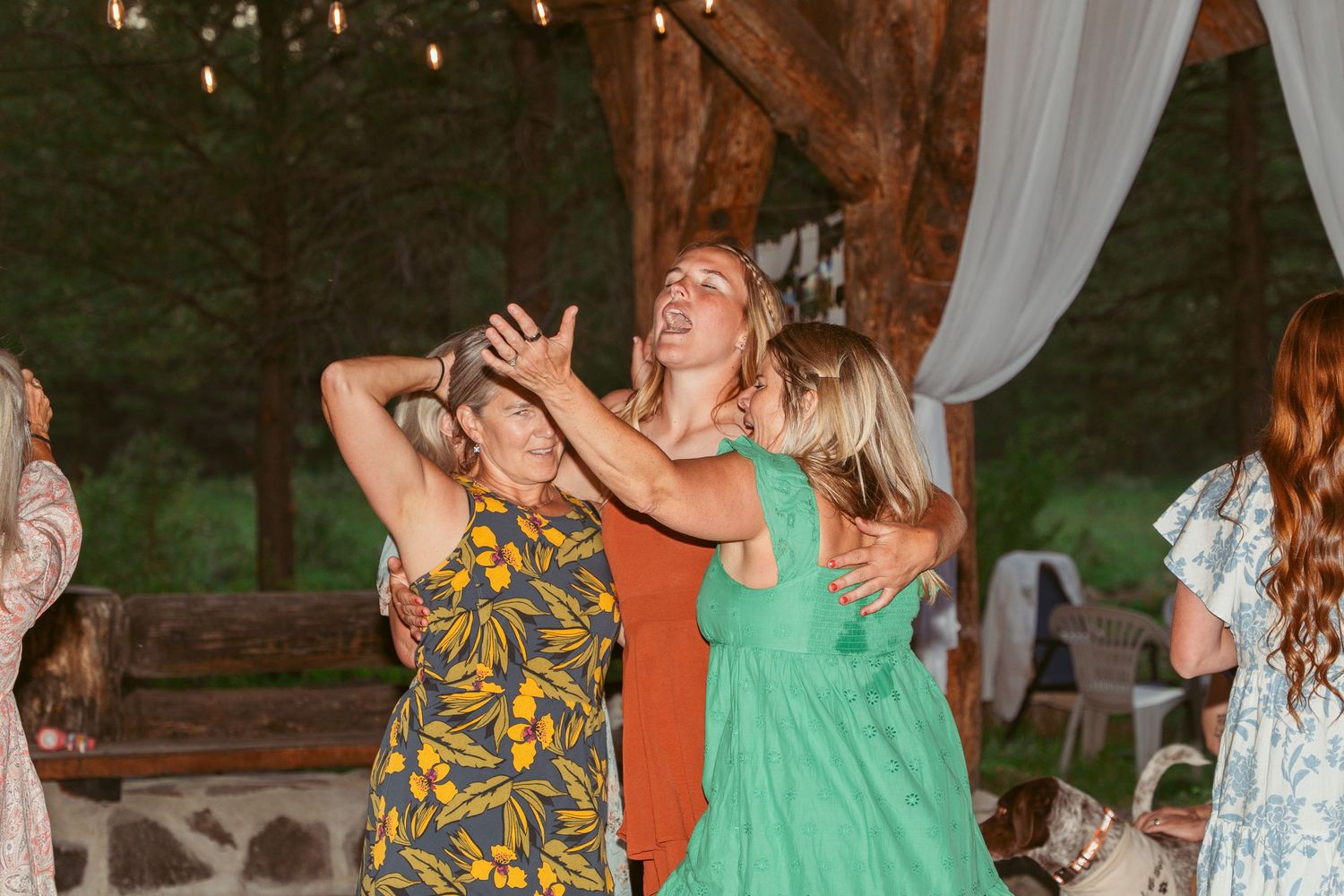 Wedding guests dancing and celebrating at an outdoor reception under string lights and trees.