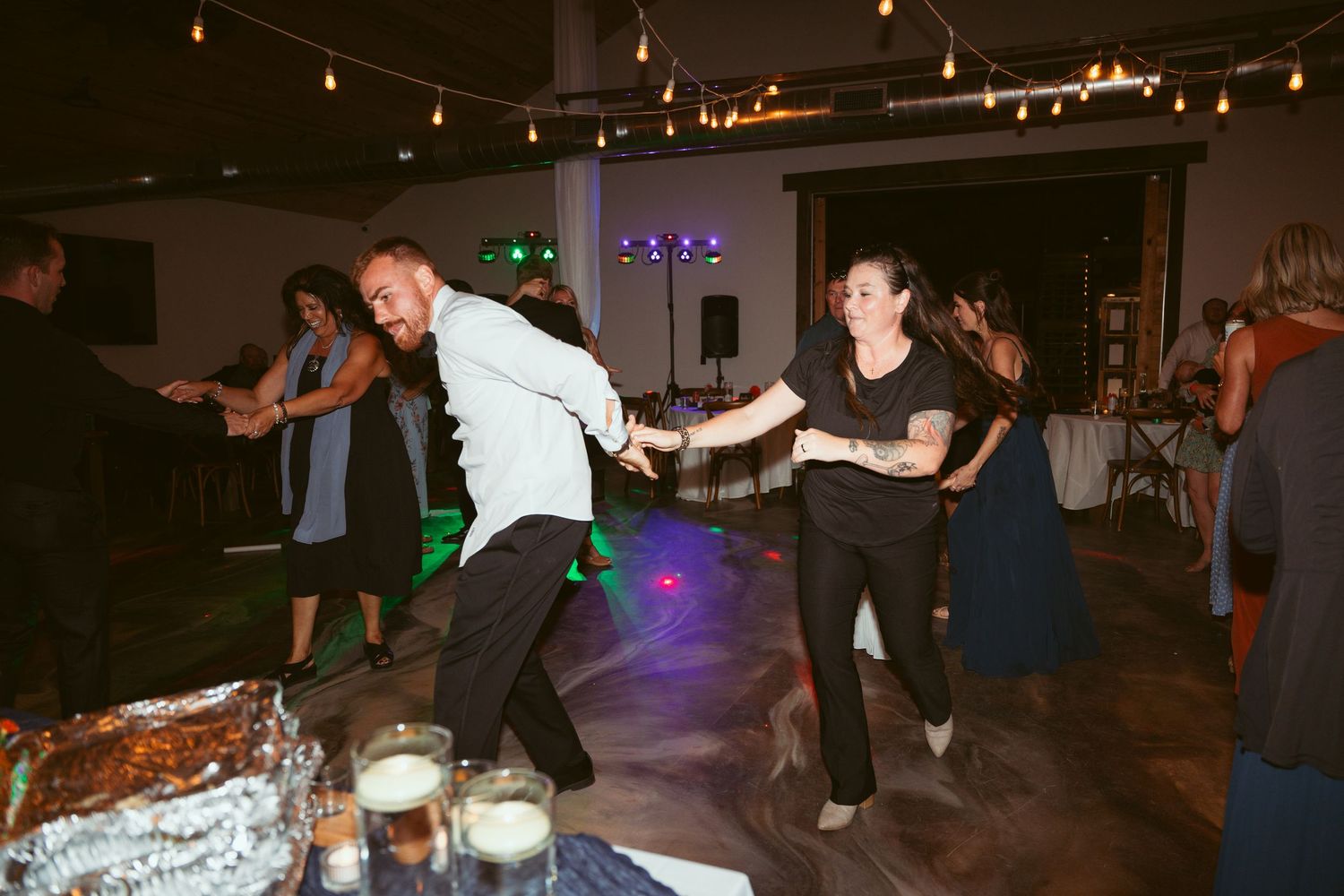Couples dancing together at a lively wedding reception with string lights overhead.