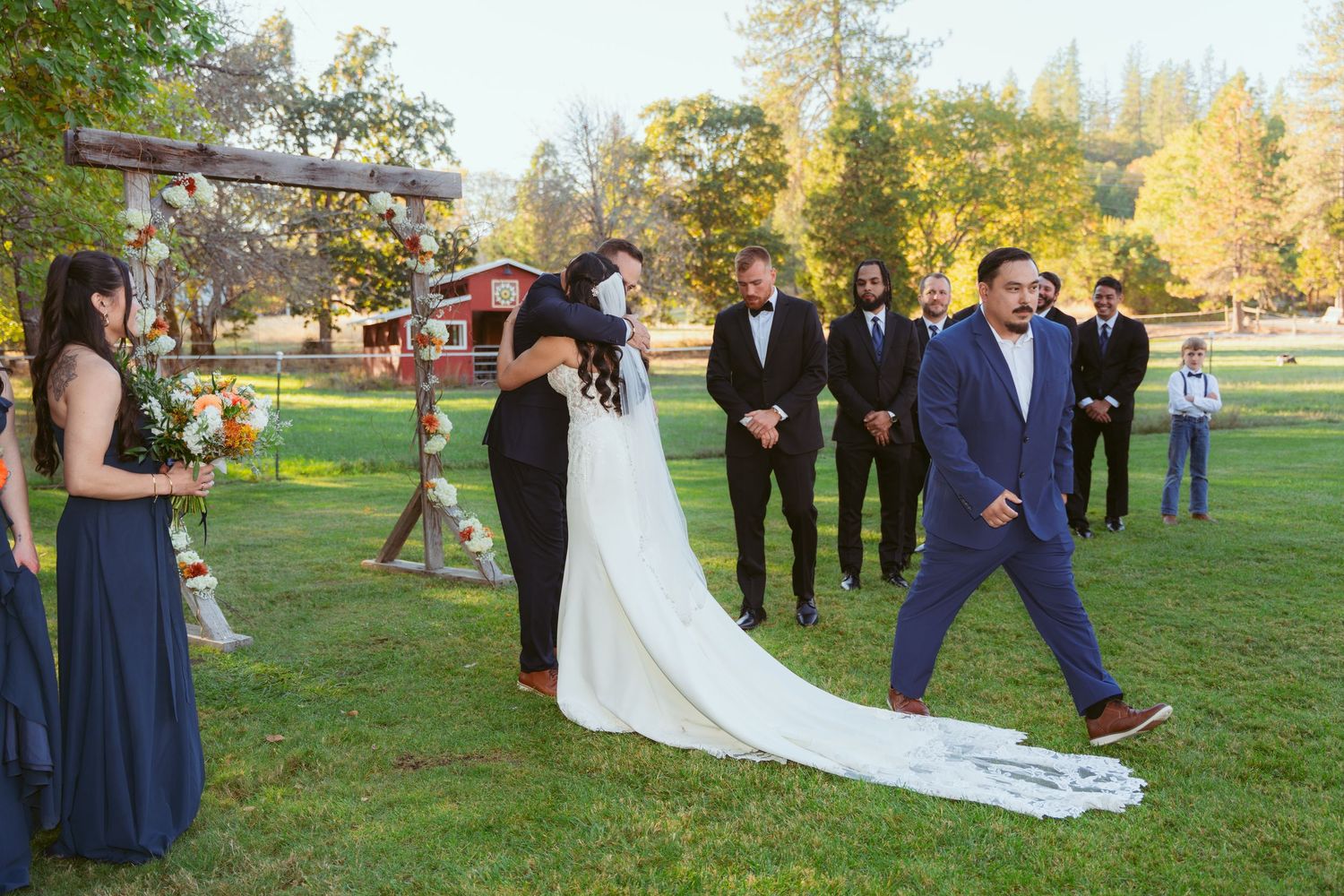 Bridal party arranged in a line on grass with autumn foliage in background.