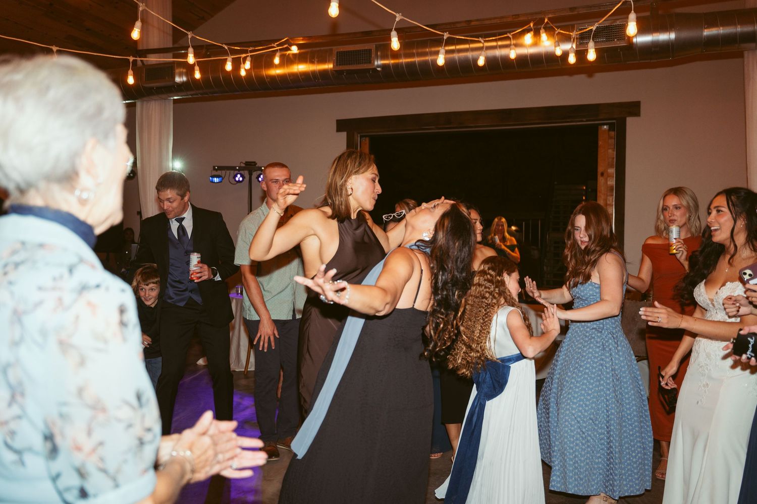 Lively dance floor scene with party guests celebrating under warm overhead lighting.