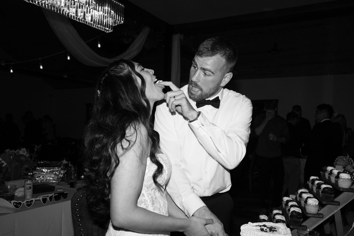 Newlyweds share laughter while feeding each other pieces of their wedding cake.