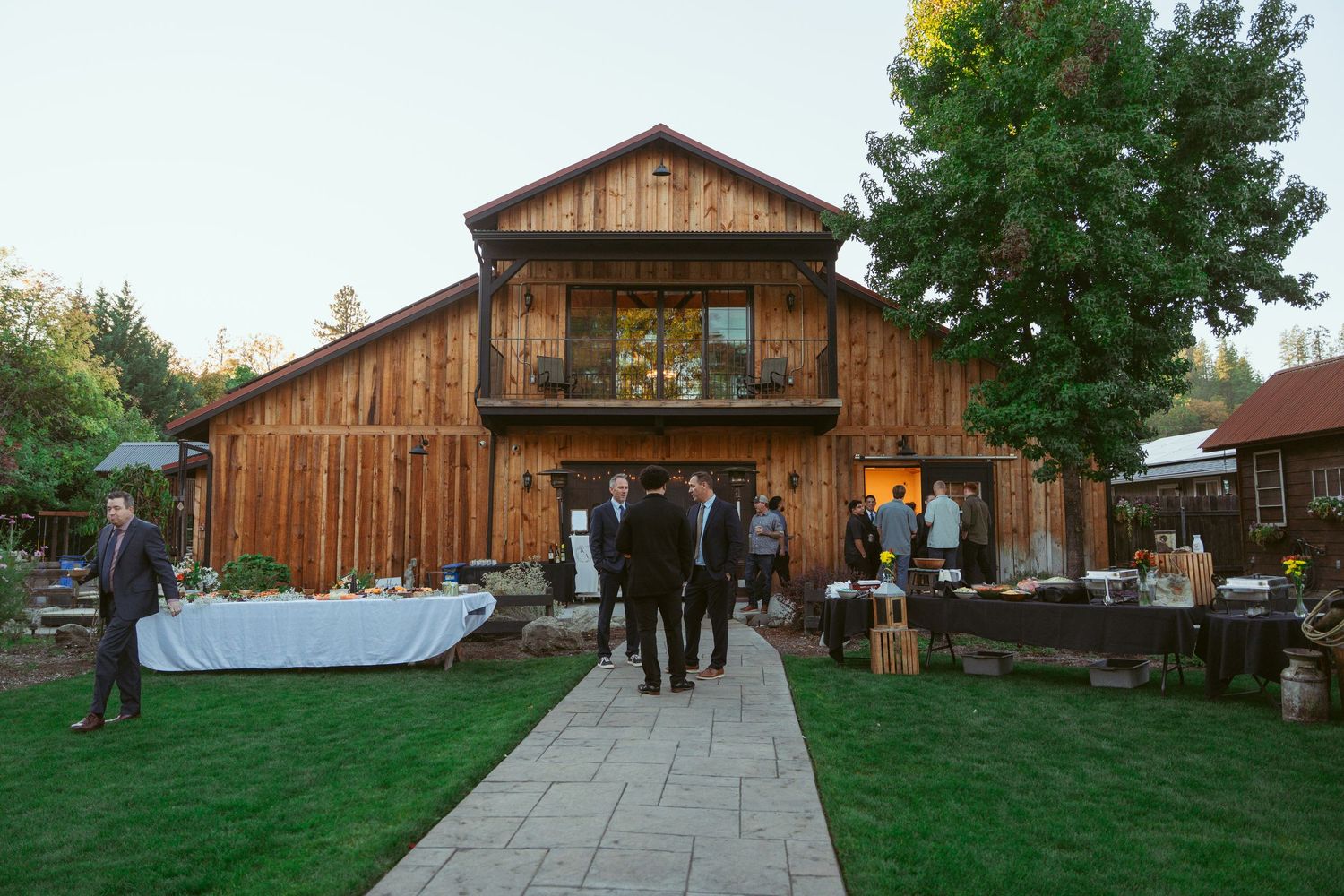 Large wooden barn wedding venue with stone pathway and outdoor reception setup.