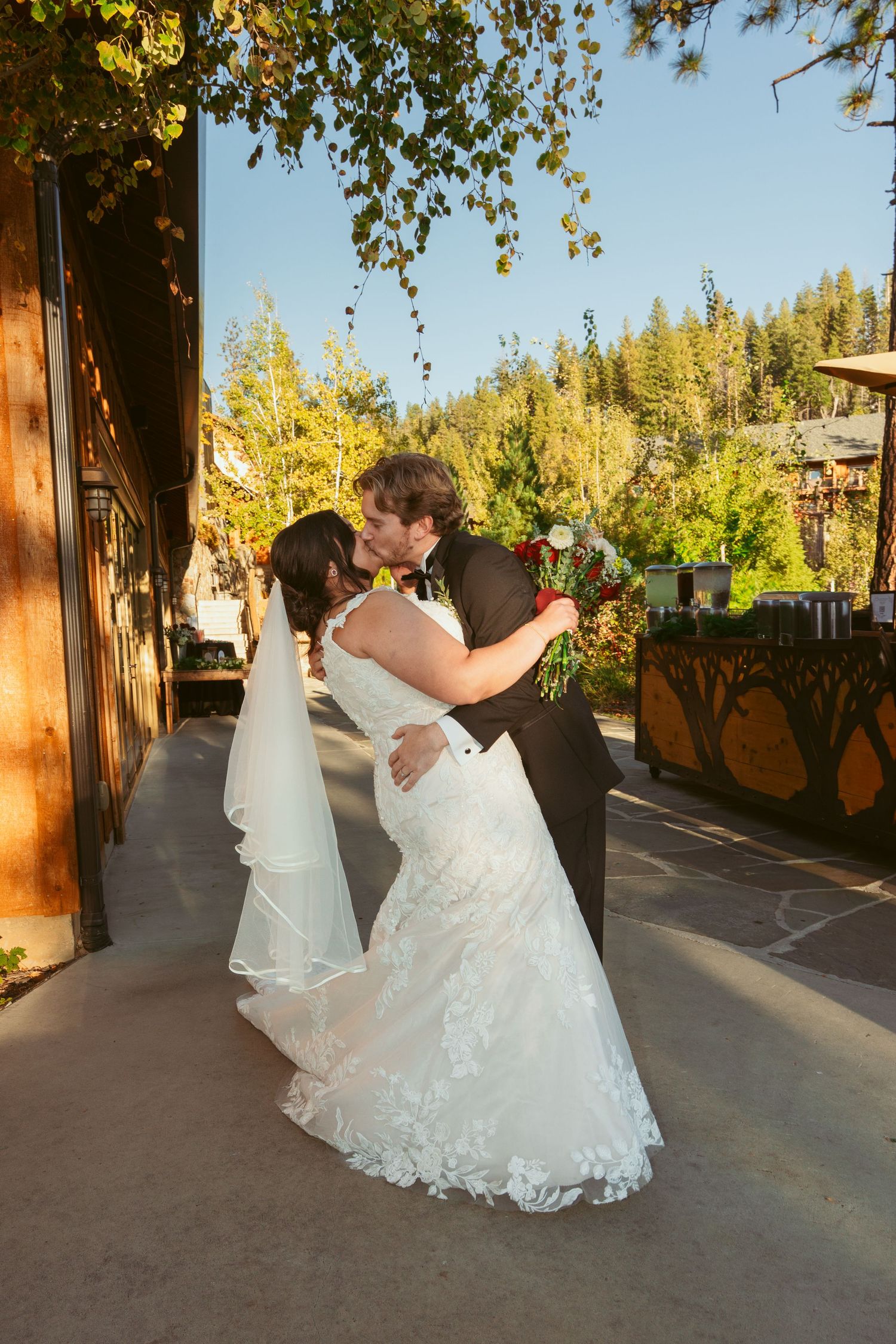 Newlyweds share a romantic dance moment on a terrace with forest scenery behind them.