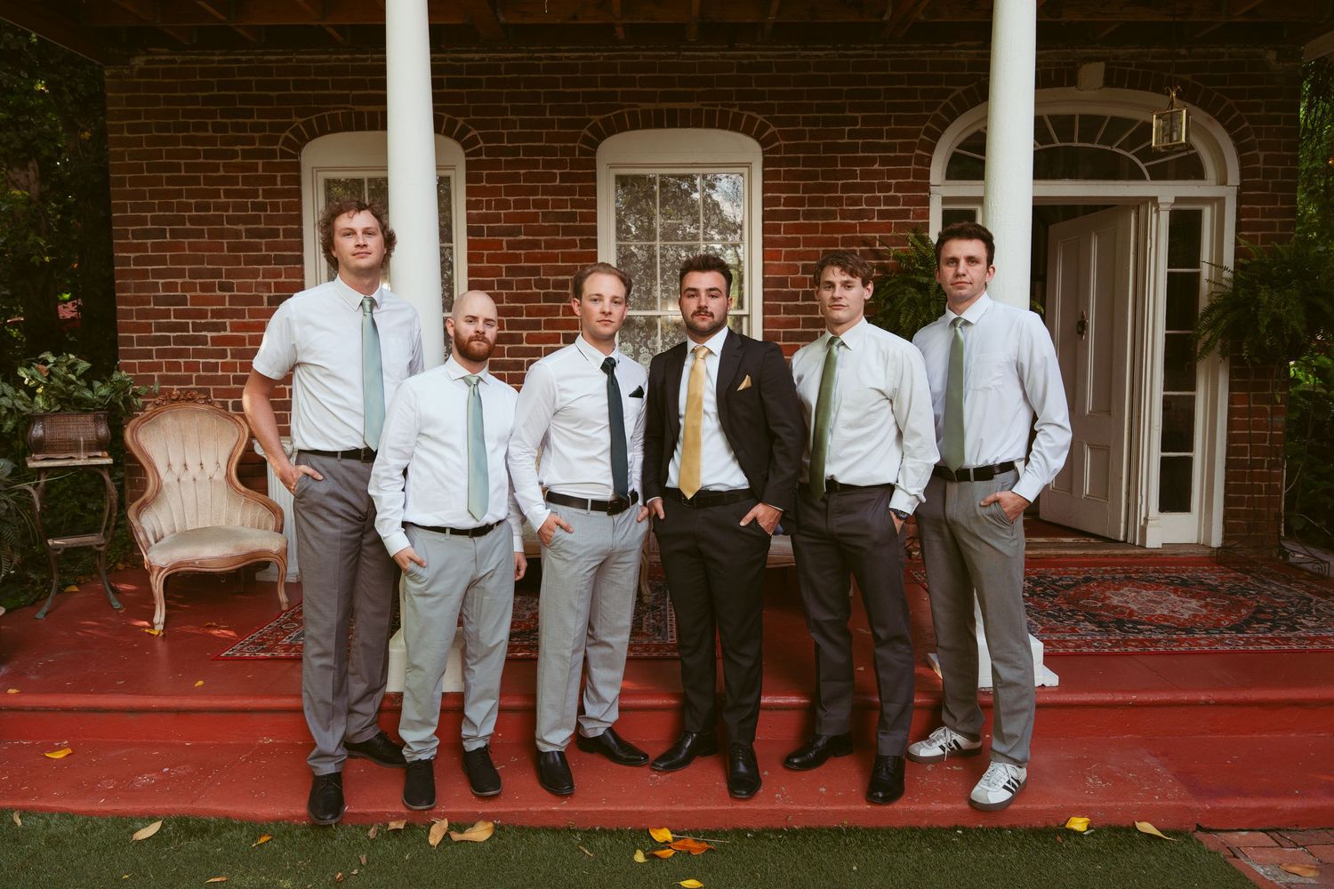 Groomsmen in gray suits and white shirts pose casually outside brick building.