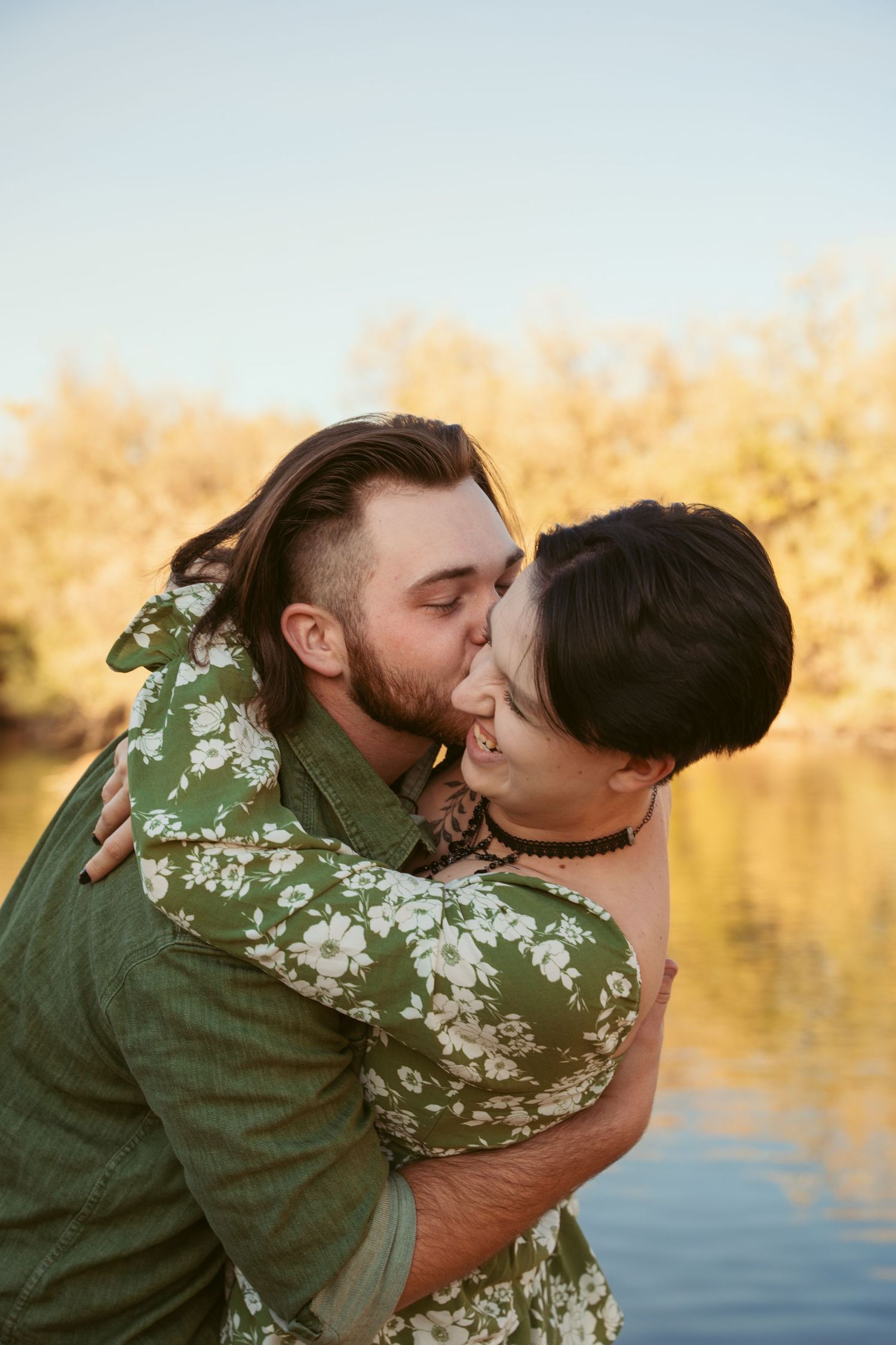 A couple shares an intimate kiss by the water during golden hour.