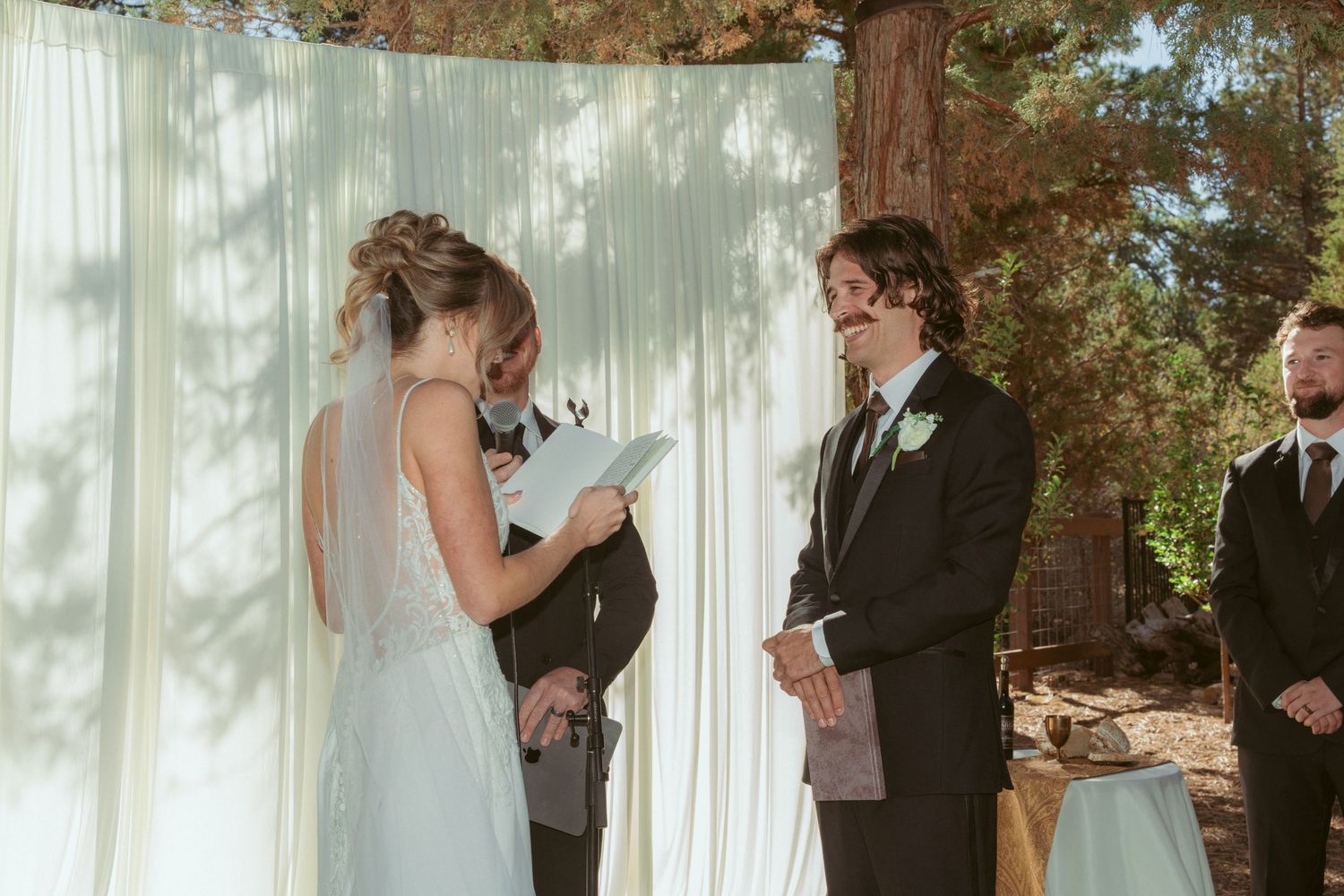 Intimate forest wedding ceremony with attendees gathered around white fabric backdrop.