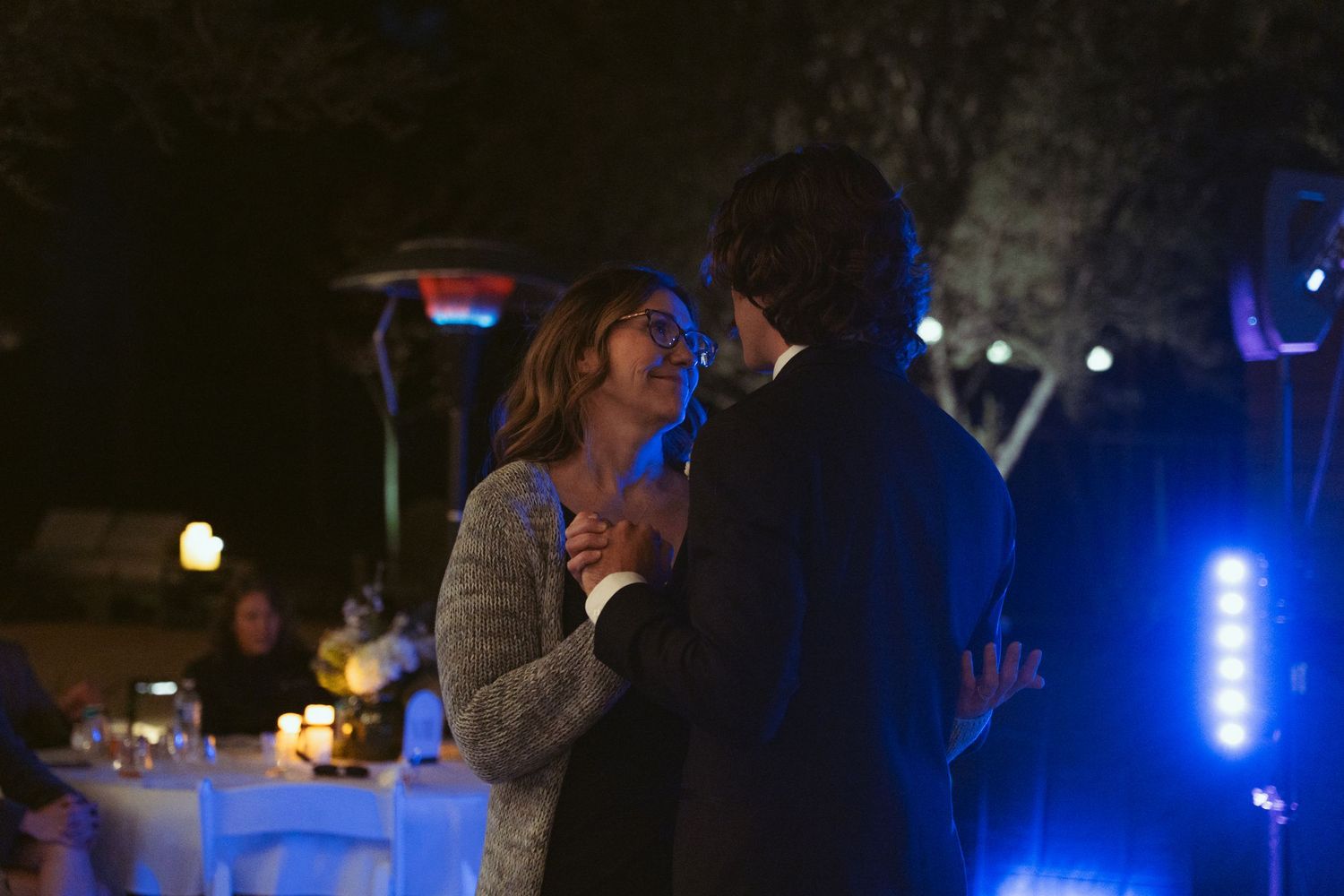 A couple dances closely together under dramatic blue lighting at an outdoor evening event.