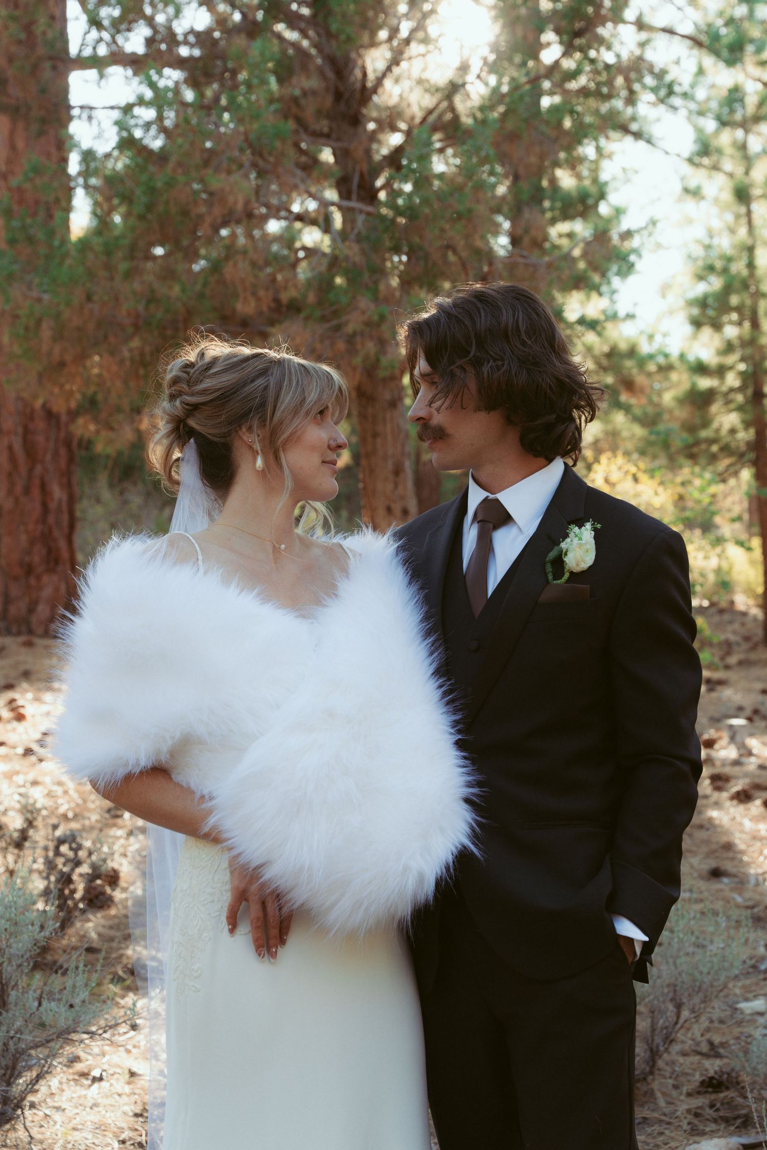A winter wedding scene with the bride wearing a white fur wrap in a forest setting.