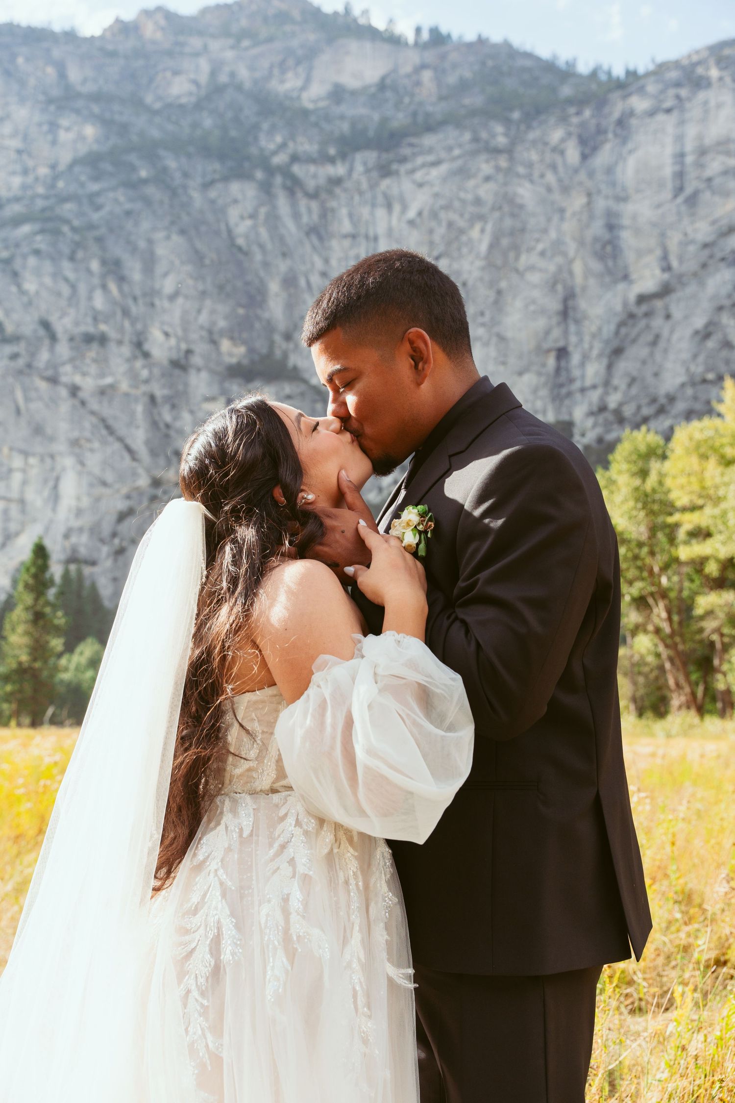 Couple sharing romantic moments in a golden meadow with Yosemite's granite cliffs in the background.