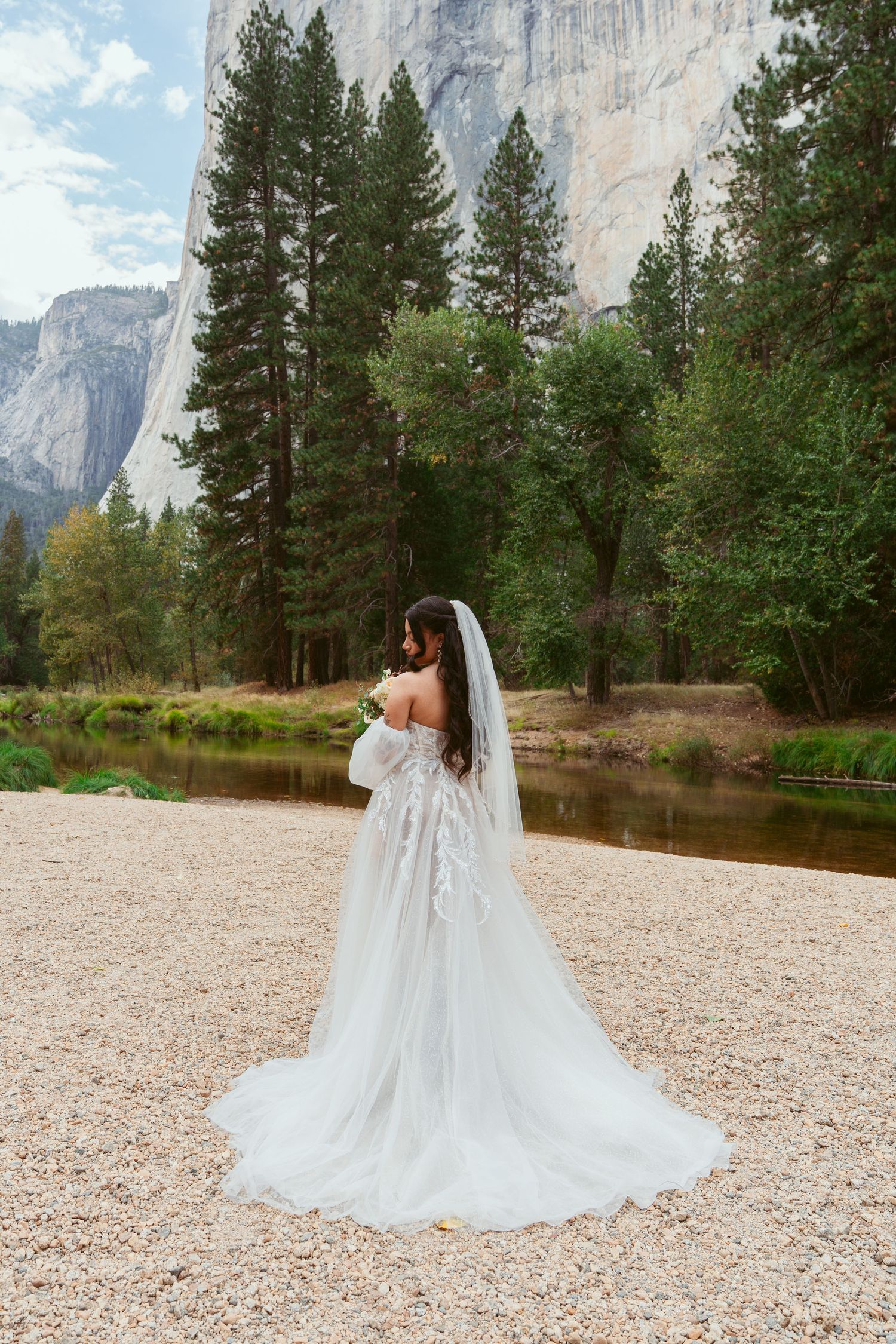 A flowing white wedding dress with a long train photographed against the majestic cliffs of Yosemite Valley.