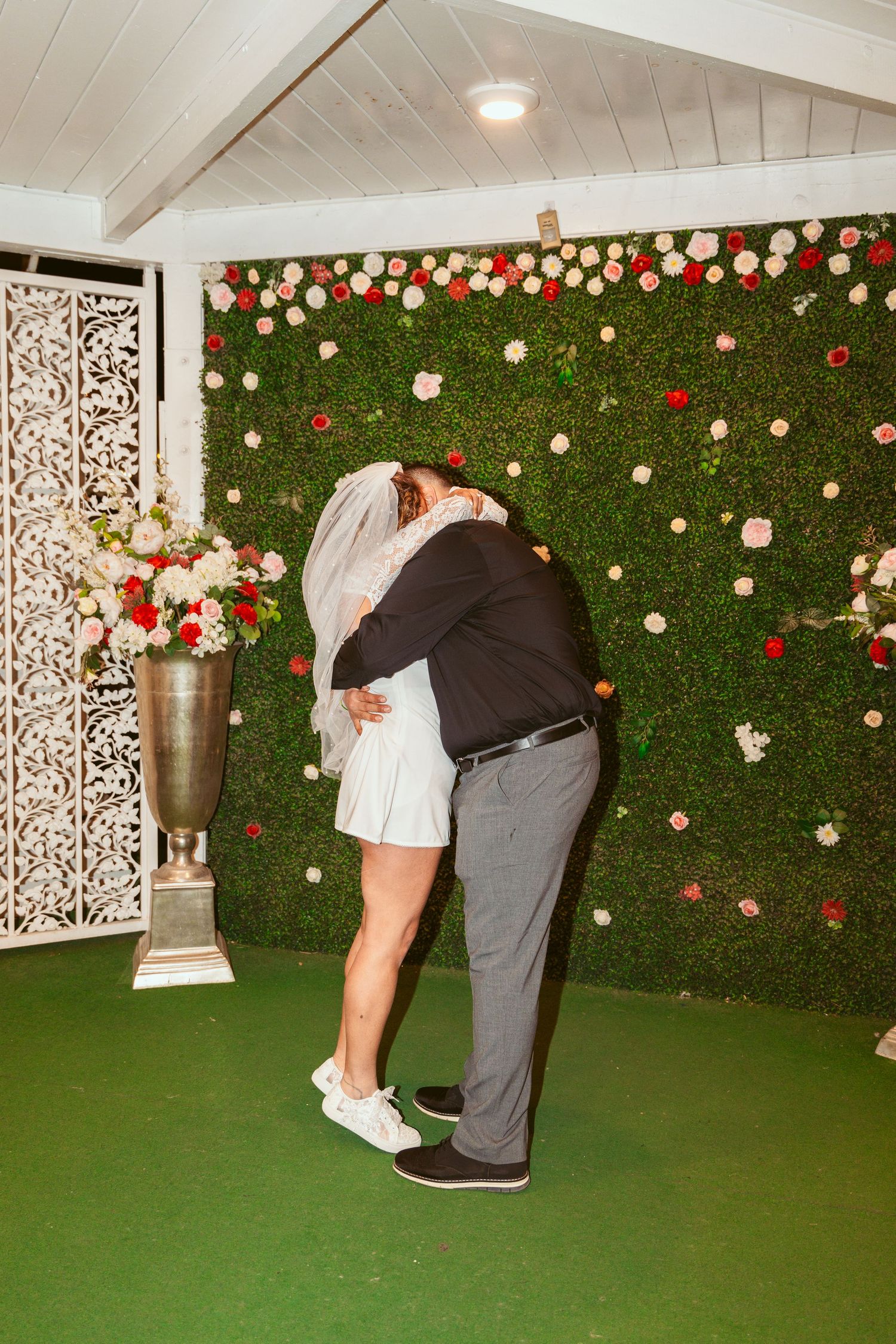 Wedding couple shares romantic moment against green hedge wall with floral decorations.